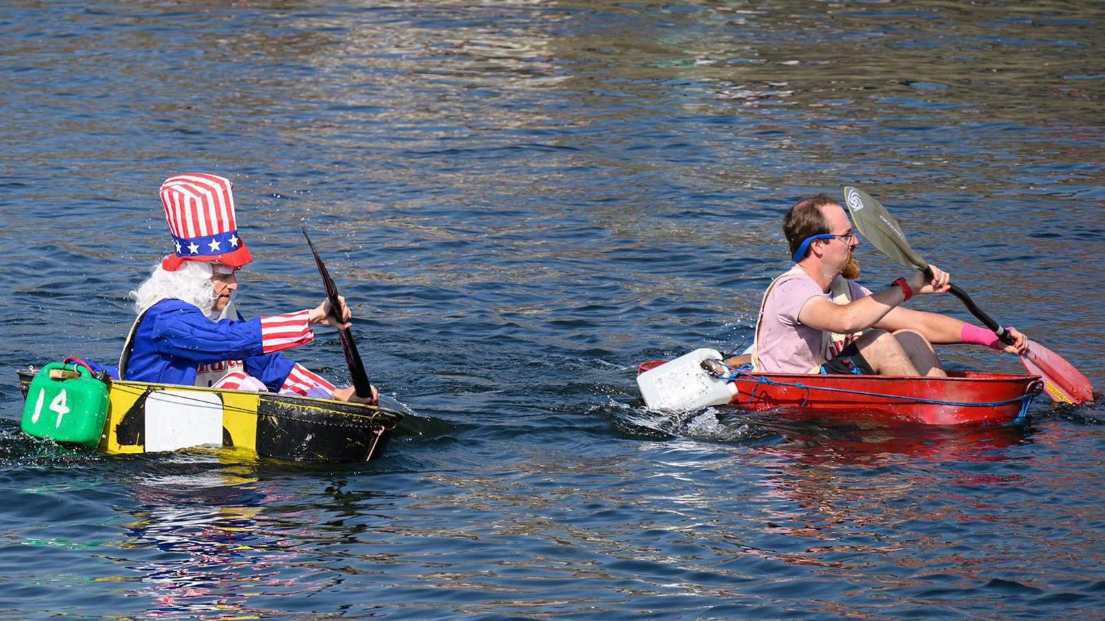 Two men paddling tin baths in the harbour, one is is fancy dress as Uncle Sam.