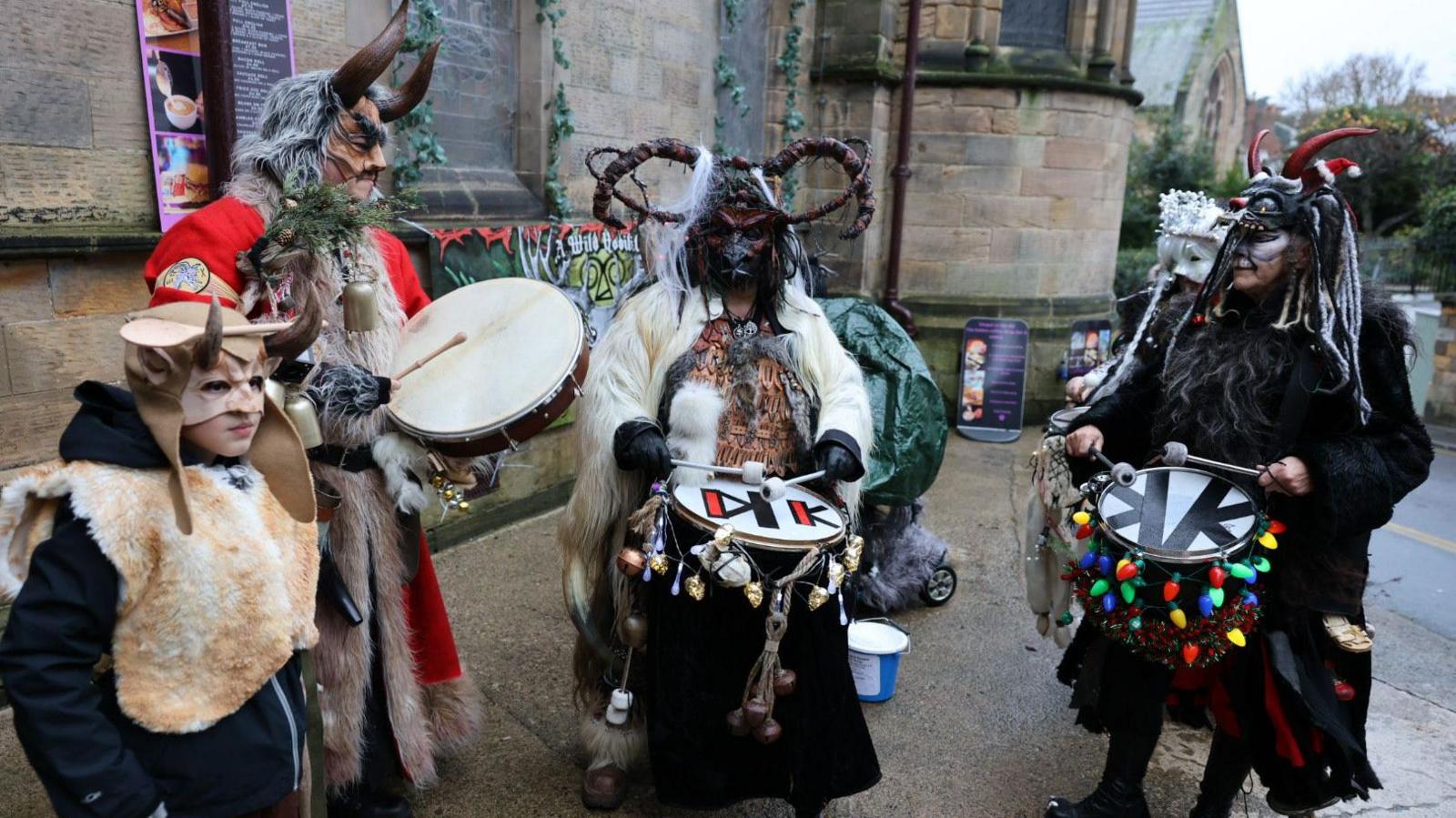 Four people dressed as Krampus, a horned beast, wearing furs and masks and drumming in a street in Whitby 