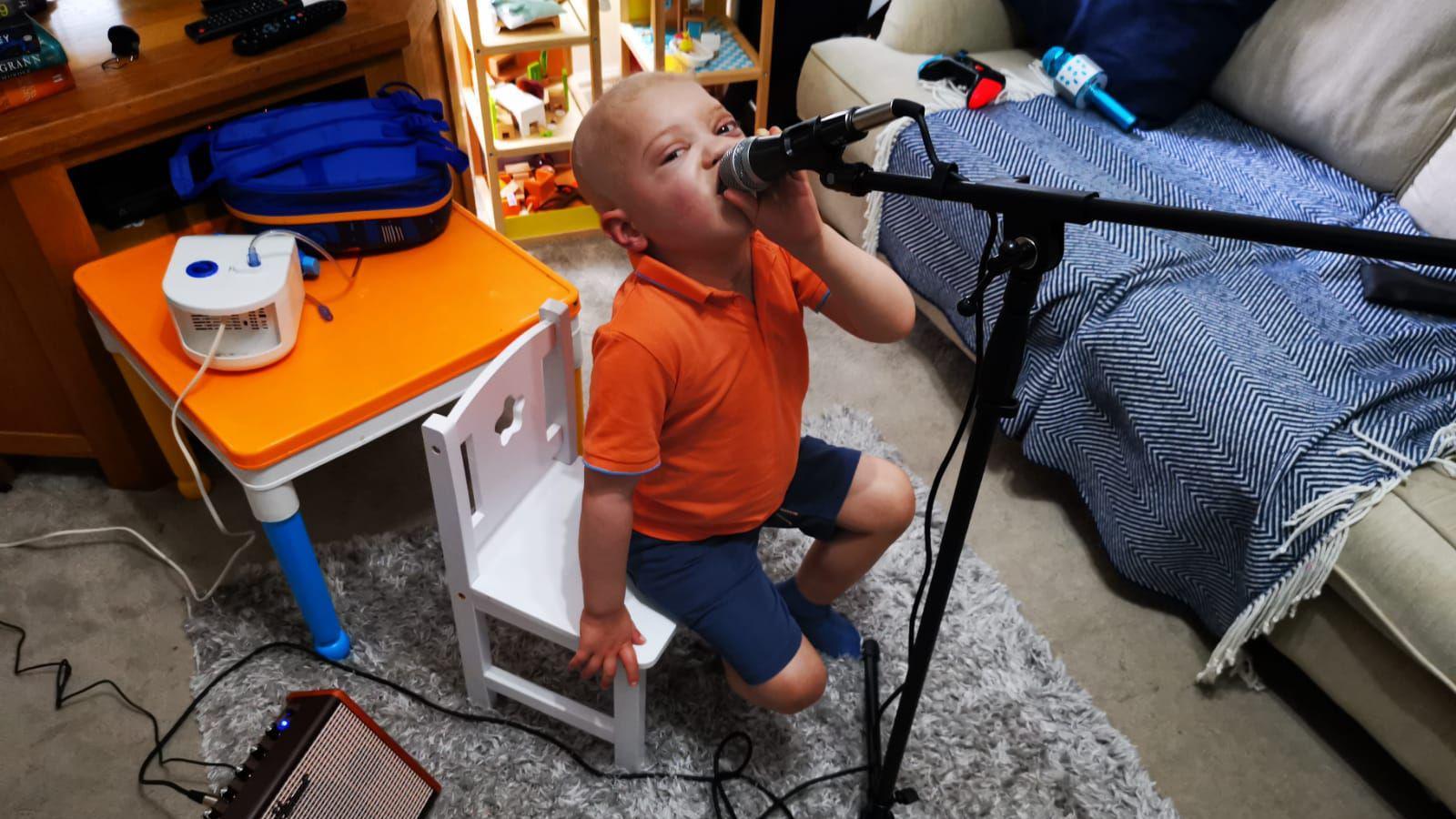 Sebastian dressed in an orange polo singing into a microphone