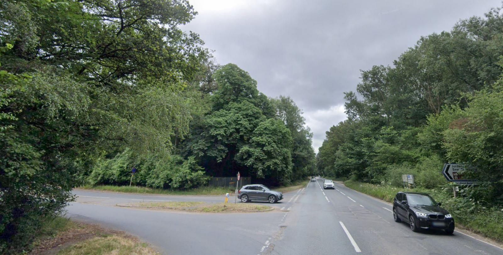 A T-road junction with a grassed island and trees and bushes surrounding the roads.