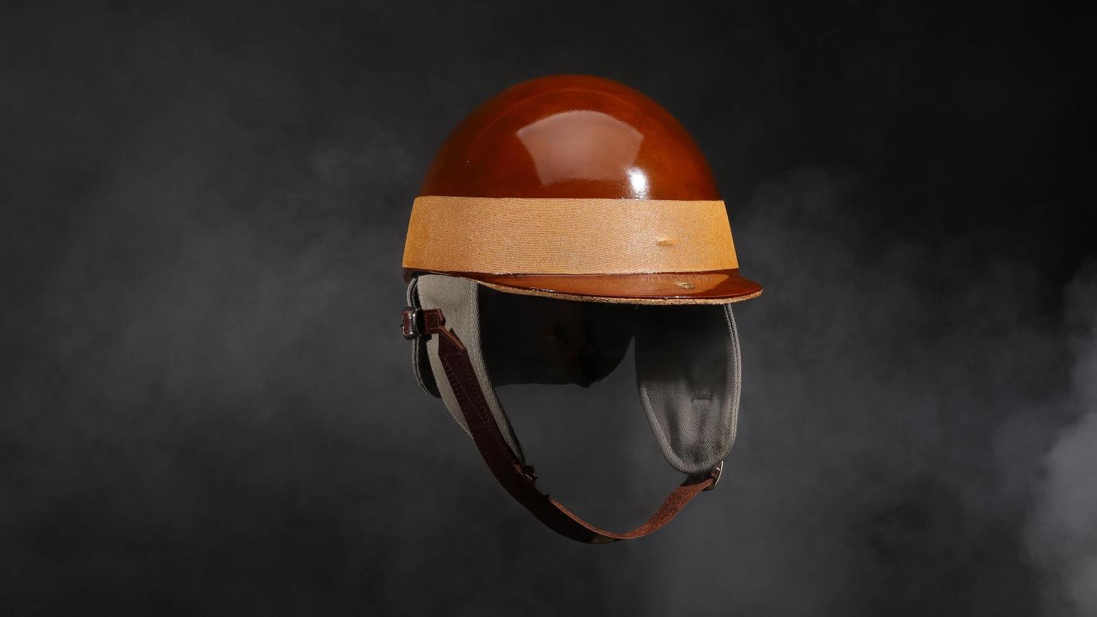 Replica 1950s-style racing helmet. It is brown with a light brown strap around the base with a brown leather chin strap.
