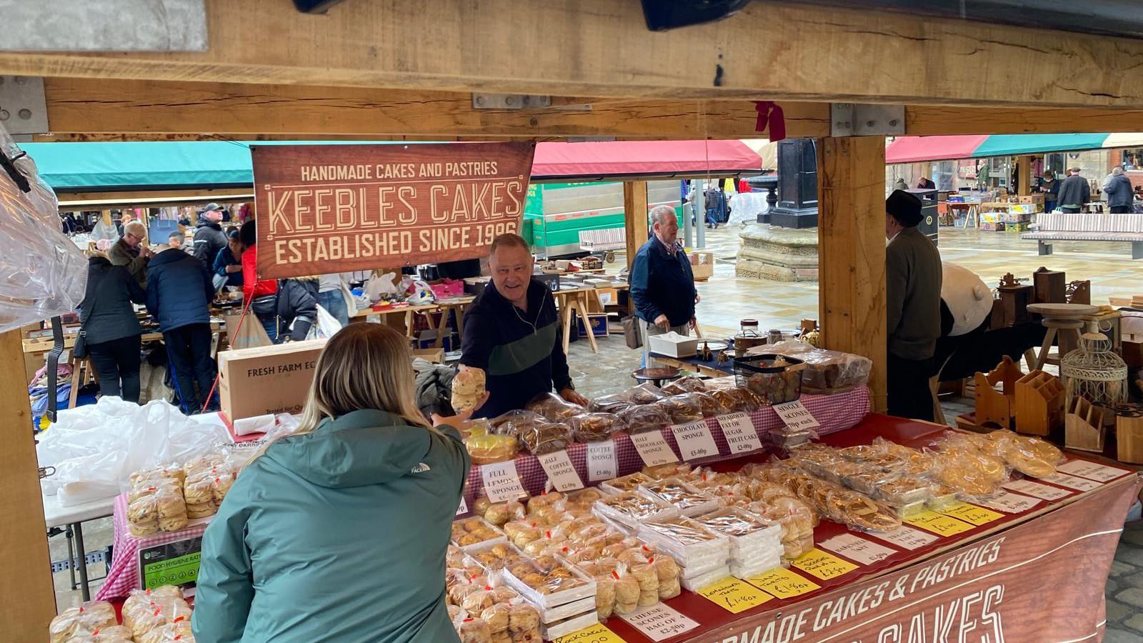 A market stall, where a man is selling cakes and breads