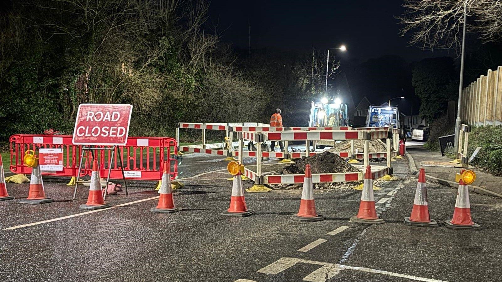 Workmen and signs on a road where there are mounds of earth as gas pipe is dug up