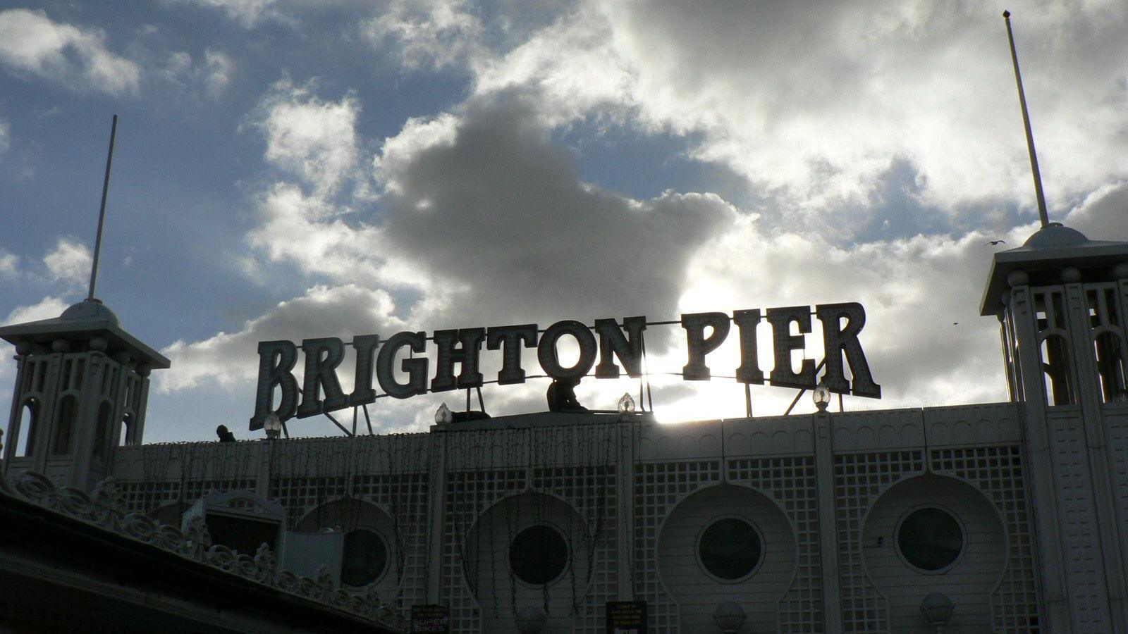 The Brighton Pier sign seen silhouetted against a backdrop of white clouds in a blue sky