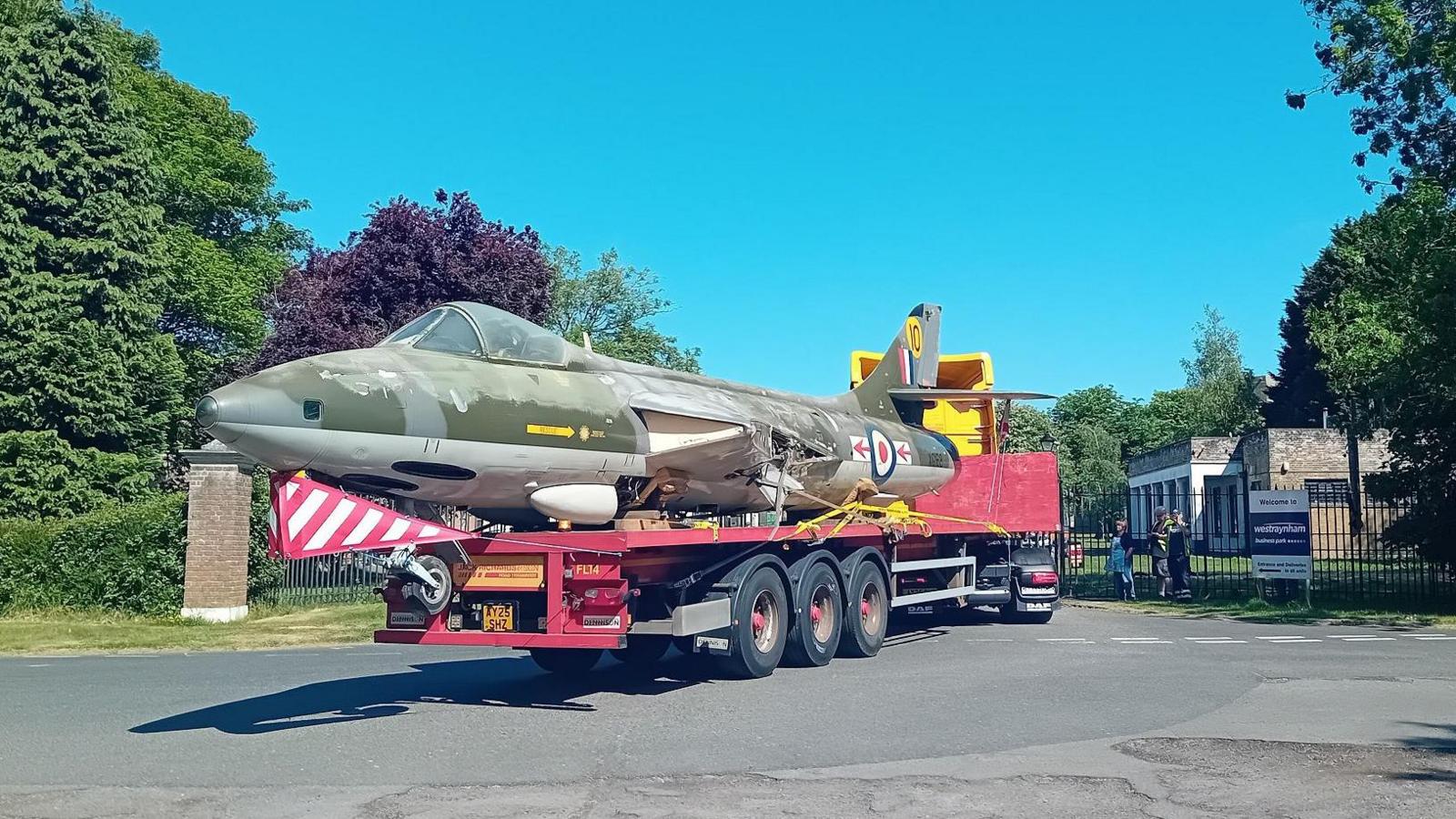 Lorry with the wingless jet being transported out of a gate.