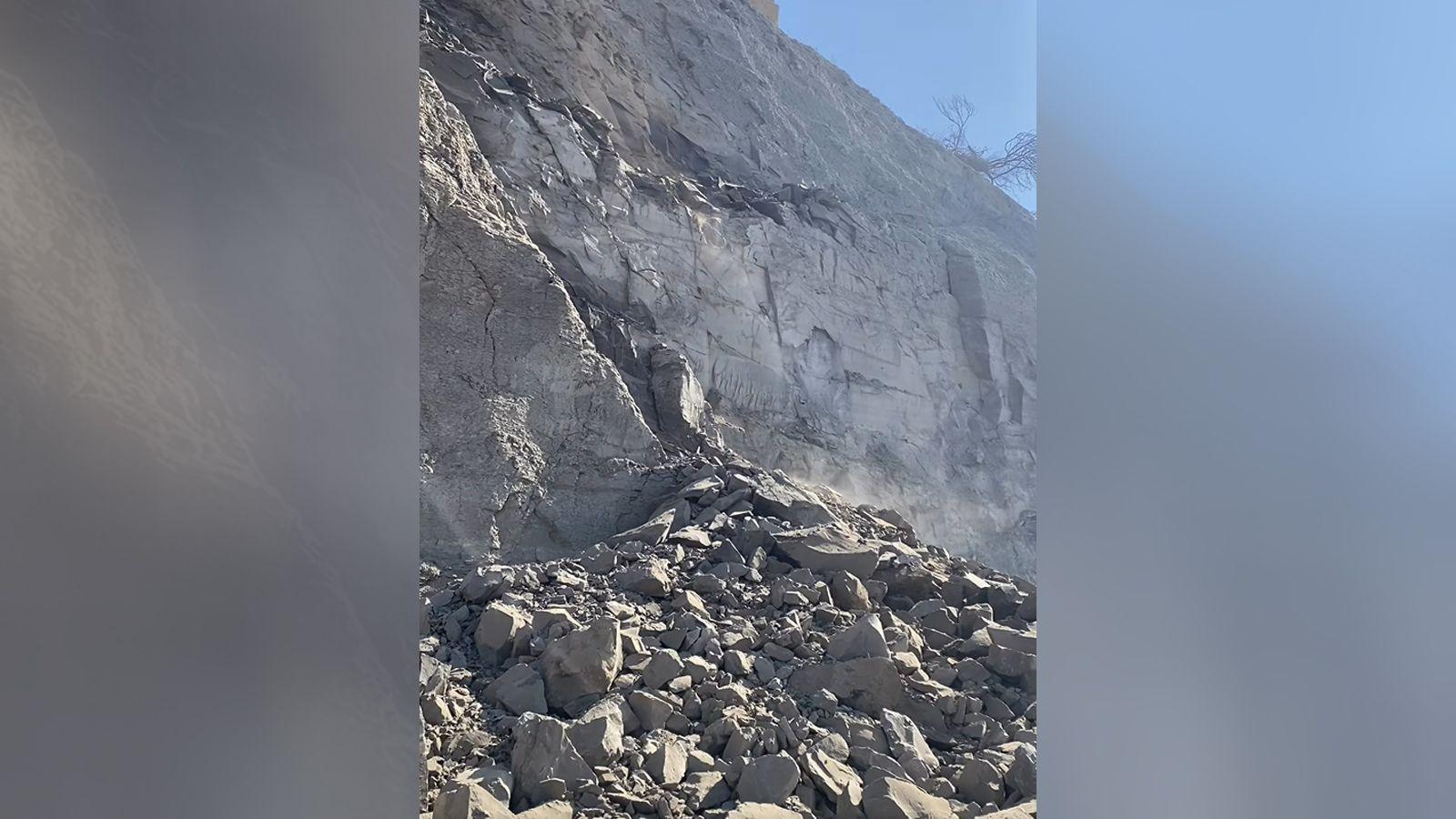 A huge pile of smashed rocks at the base of a grey crumbling cliff