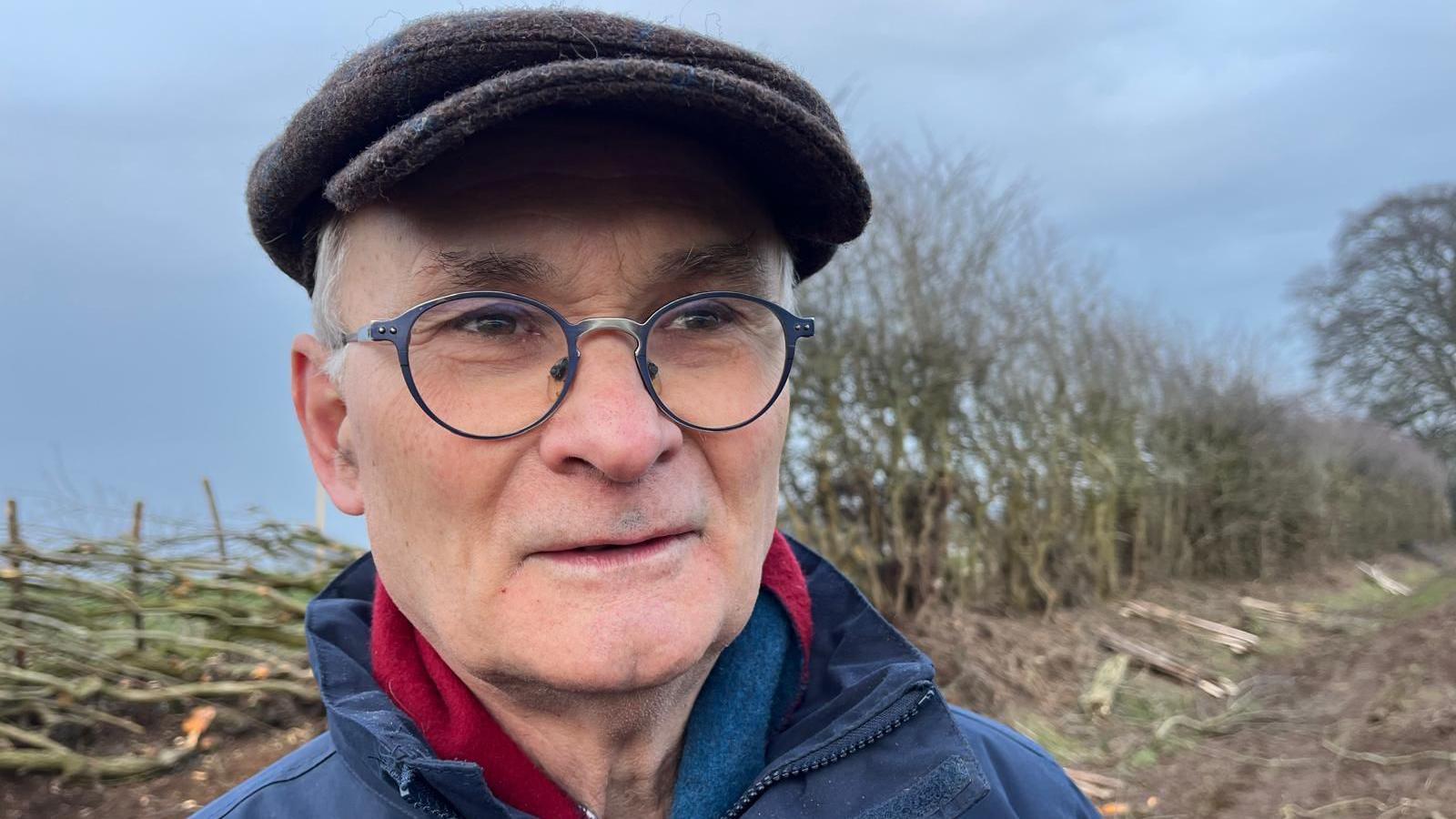 John faces the camera with a half laid hedge behind him 