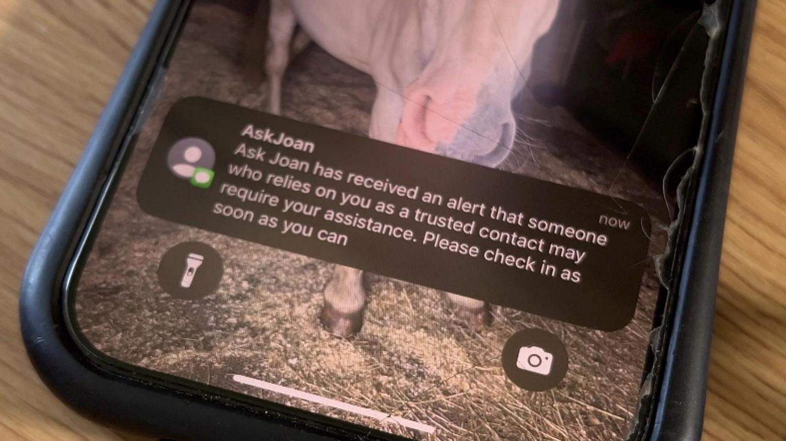 The screen of a smartphone displays a message from Ask Joan, telling the recipient to check in with the sender as soon as possible