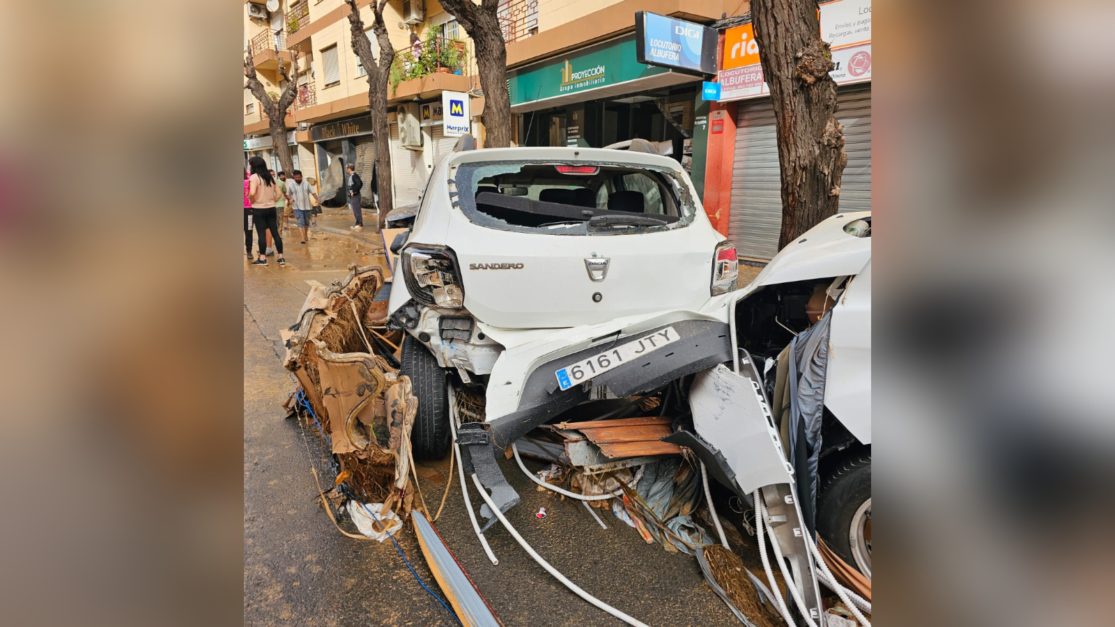 A white car is wrecked after flooding in Valencia. The back of the car is crumpled and the back window is missing. 