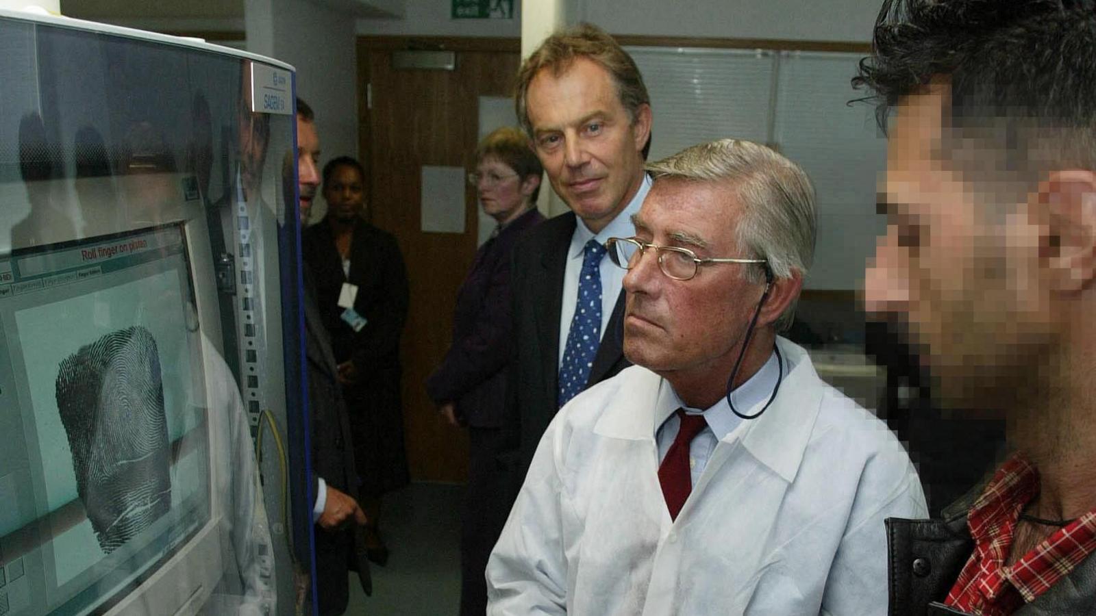 Tony Blair watches an asylum seeker get his finger prints taken in 2003