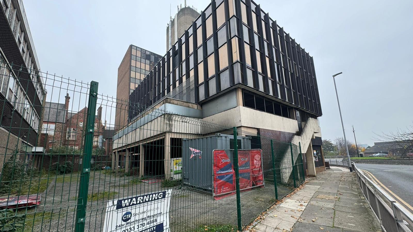 Redundant buildings around Gladstone Street to become part of the new development. The building is a dilapidated office block surrounded by a fence.