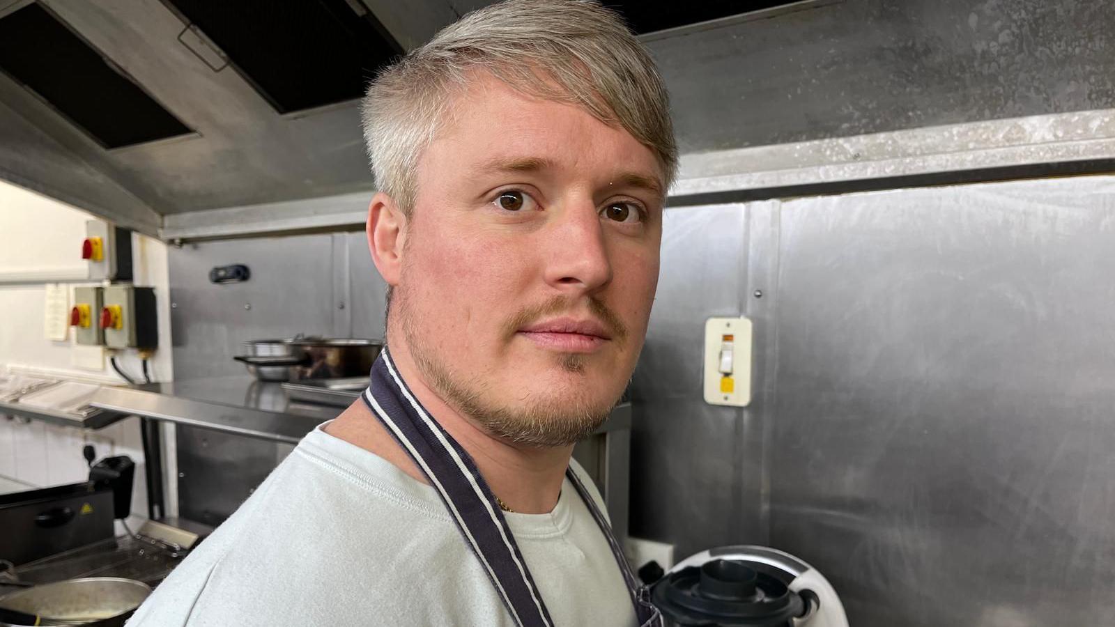 Chef, Dan Burrell, in a white t-shirt and apron in the kitchen 