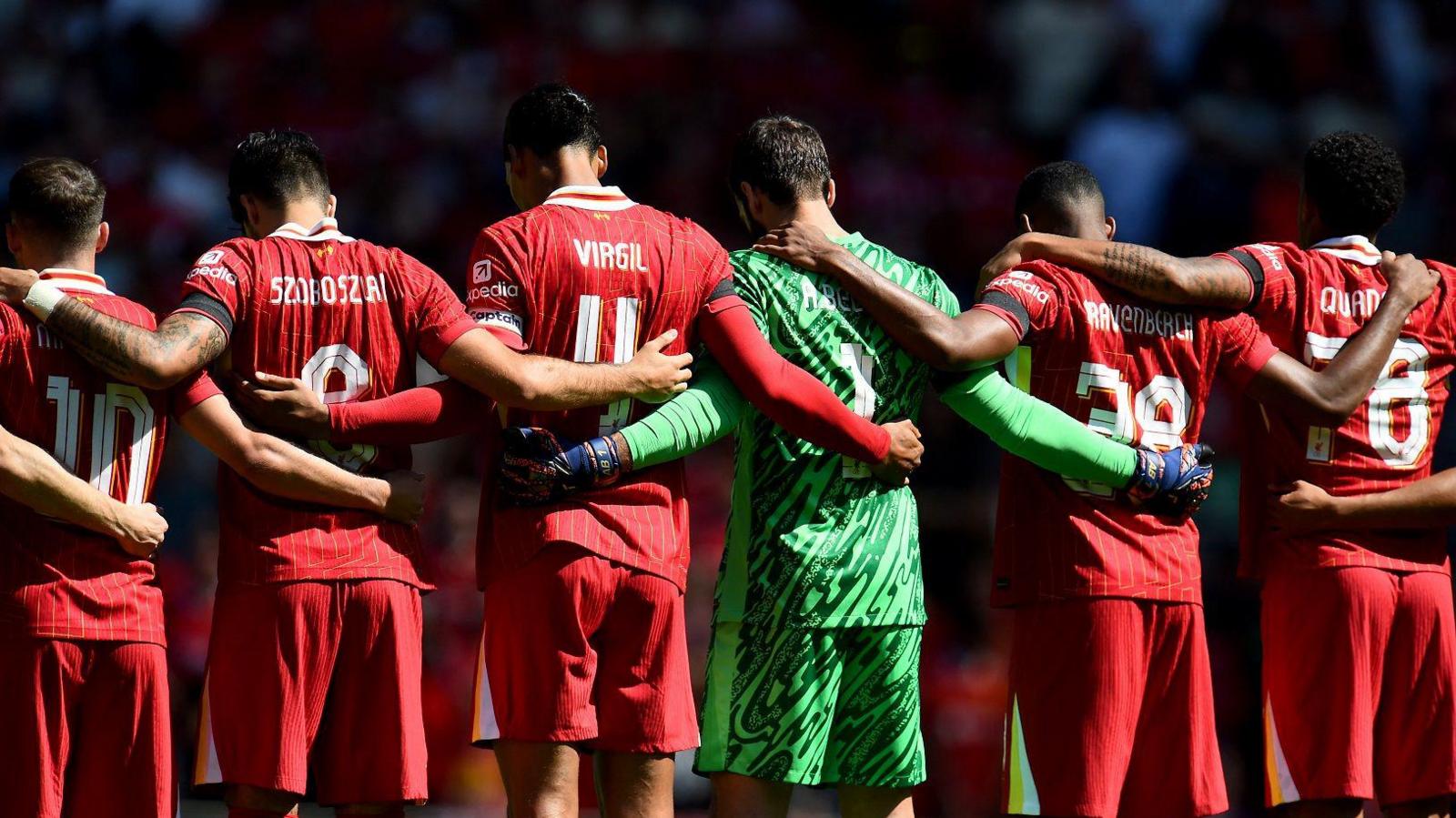 back view of Liverpool players clasping arms around each other as they hold a minute's silence