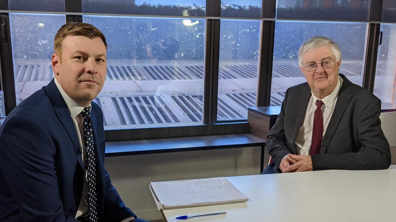 Llun o Mark Drakeford a gohebydd gwleidyddol BBC Cymru Cemlyn Davies yn eistedd wrth bwrdd. Mae'r ddau'n edrych tuag at y camera.
