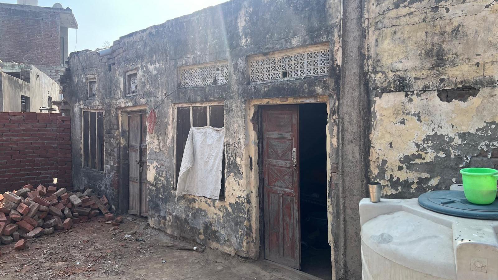 A dilapidated building with paint peeling off the walls and piles of bricks outside.