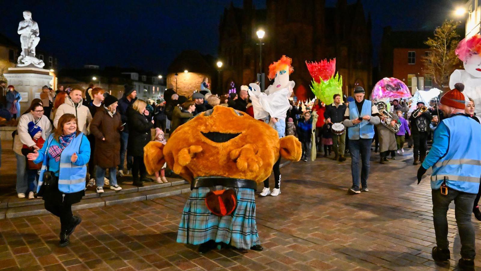 A cuddly haggis in a kilt leads the Big Burns Supper parade through Dumfries with a statue of Robert Burns in the background