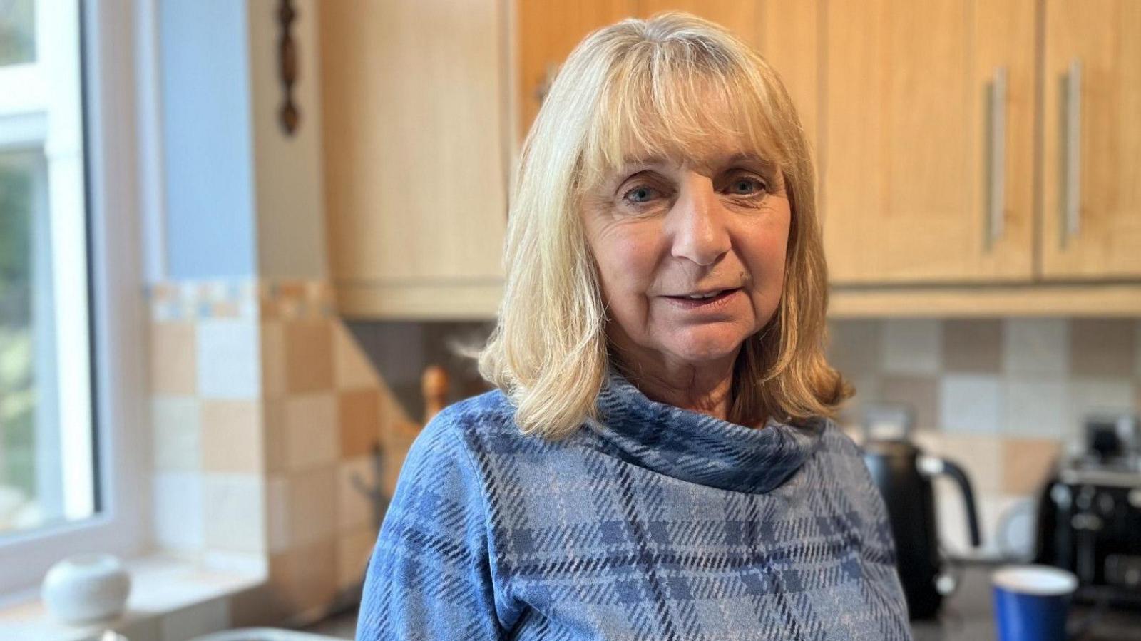 Blonde woman in blue top standing in a kitchen 