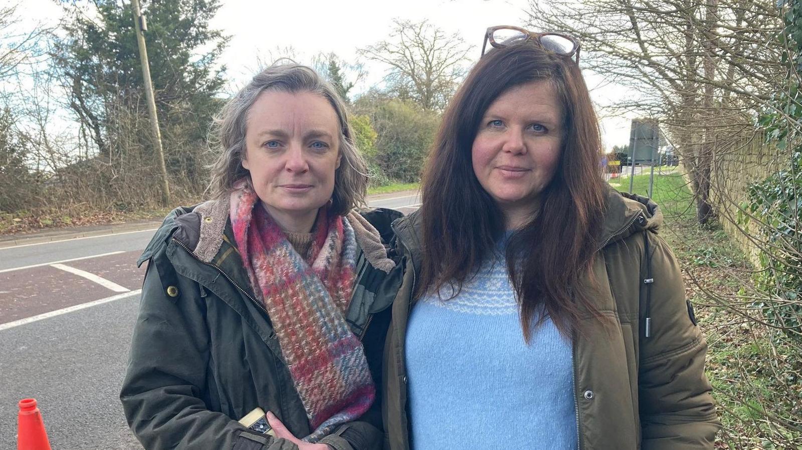 Harriet (left) and Sam stand beside the road, both wearing winter coats and smiling slightly at the camera. 