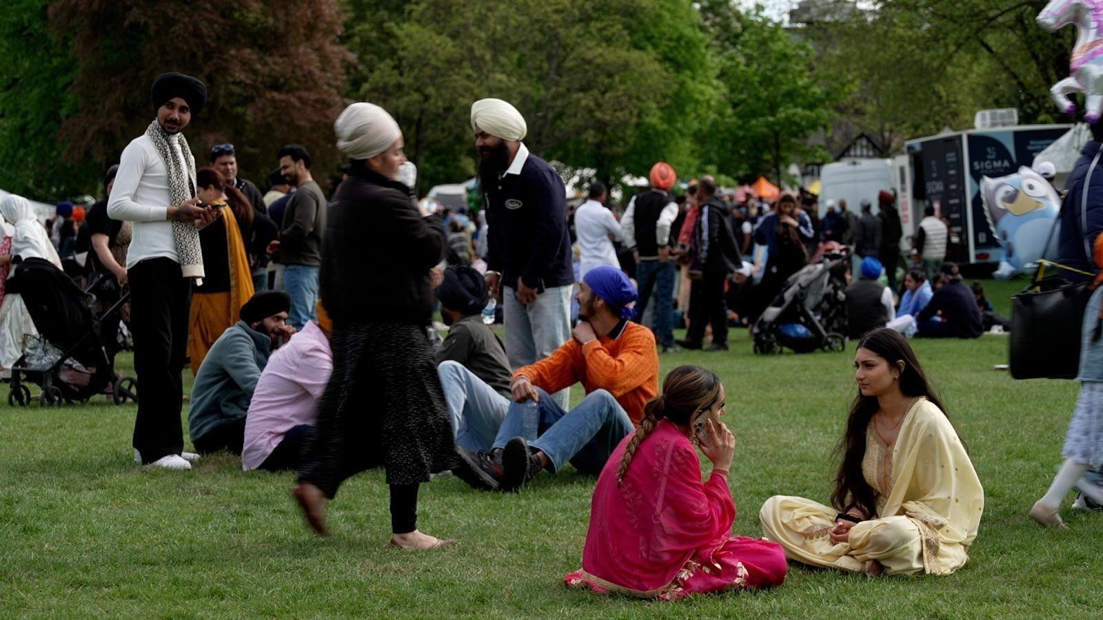 Crowds of people sitting and standing on the grass in a park.