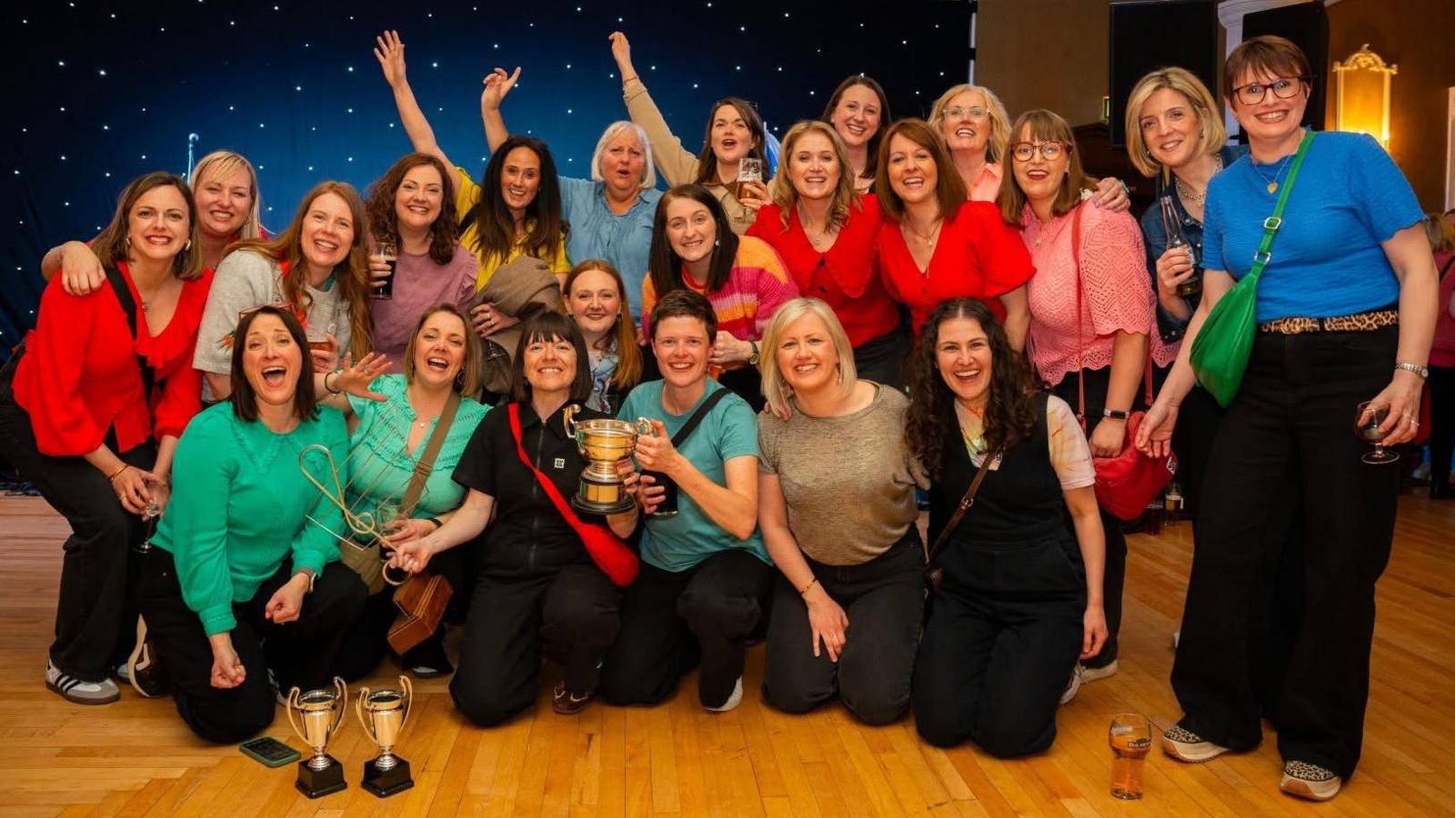 Merched Soar yn dathlu gyda'u harweinydd Carys Mai sy'n dal cwpan y côr buddugol (chwith)