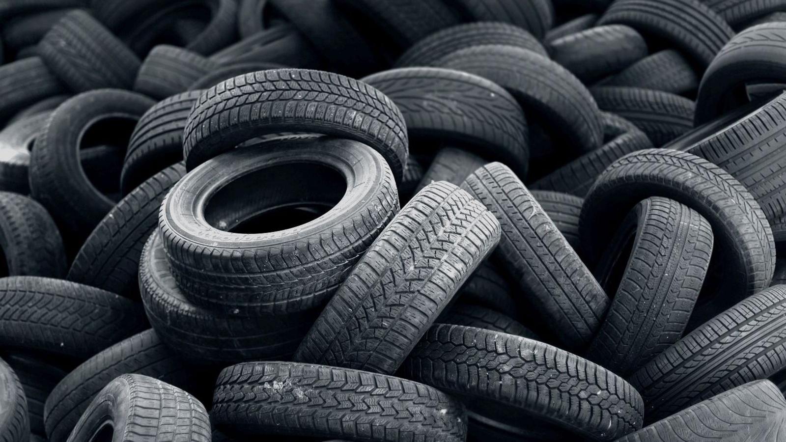 A close-up of a large pile of used tyres, arranged haphazardly, some with their word tread facing the camera, others with their sidewalls visible