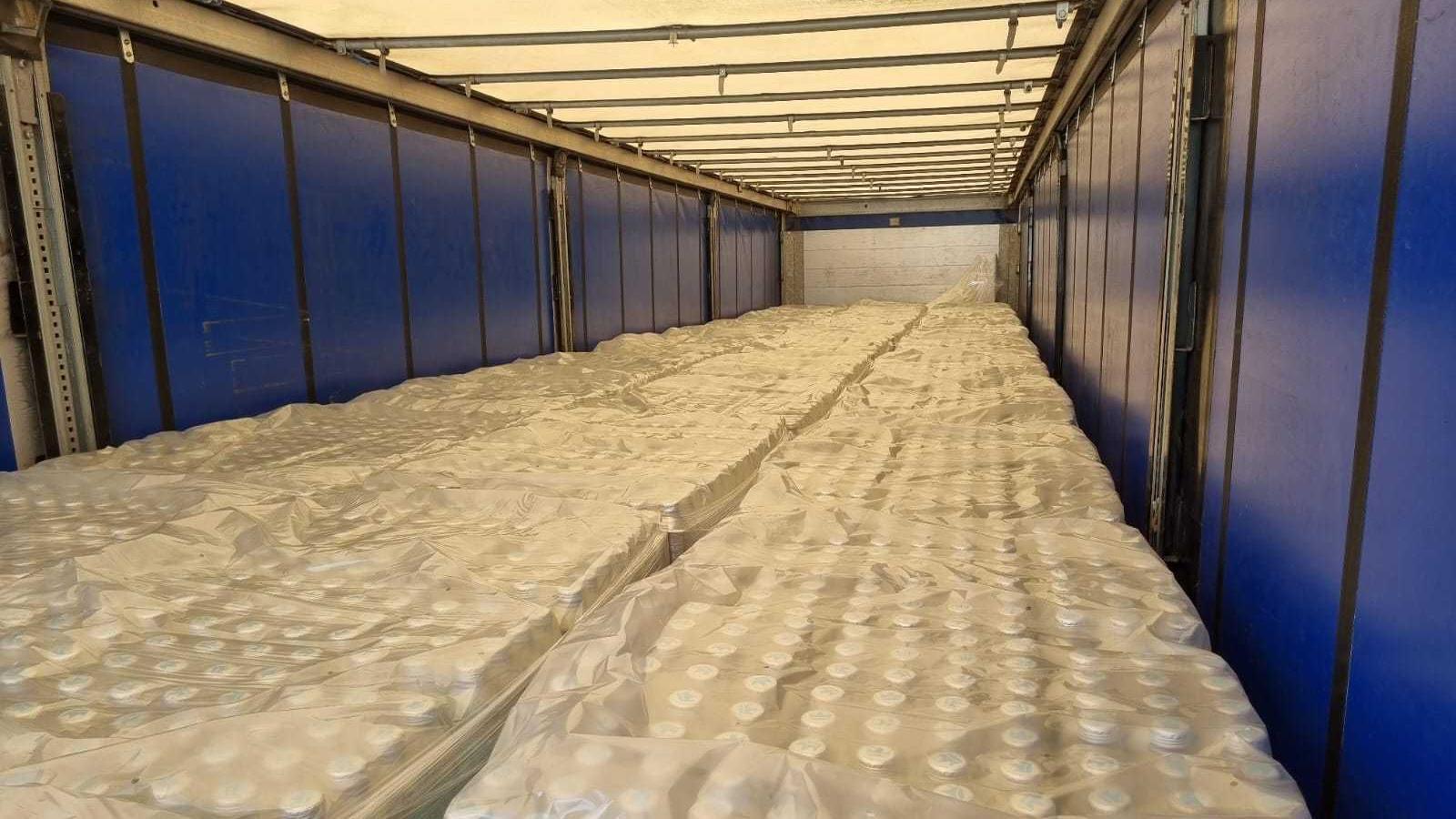 A picture taken showing the contents of the lorry as it was sealed and locked before leaving Germany. The walls of the cabin are blue and it is full with what appears to be crates of bottles wrapped in clear plastic. 