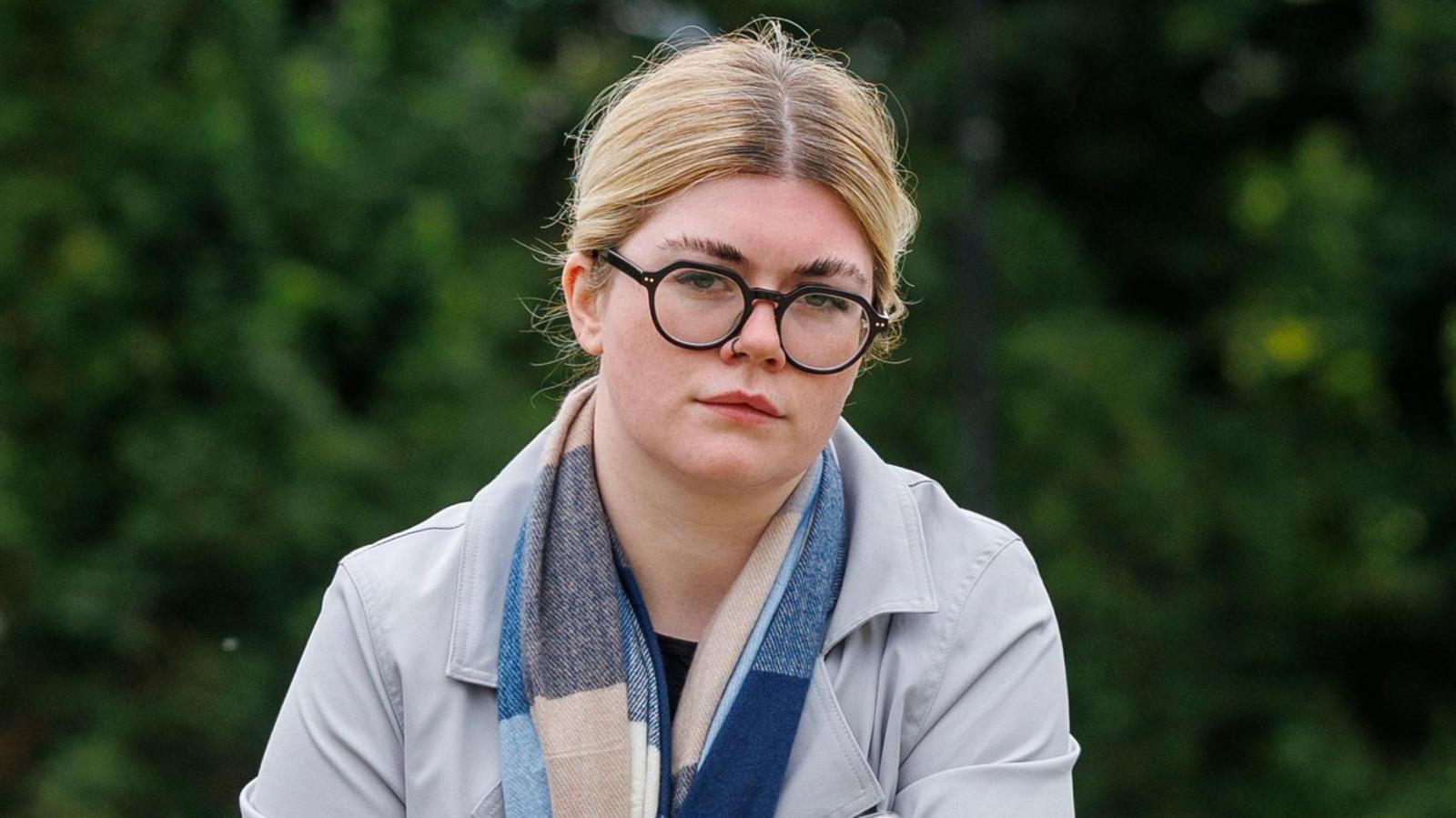 Ciara Corvan, with tied up blonde hair, wearing glasses, a blue and beige scarf and a grey jacket. 