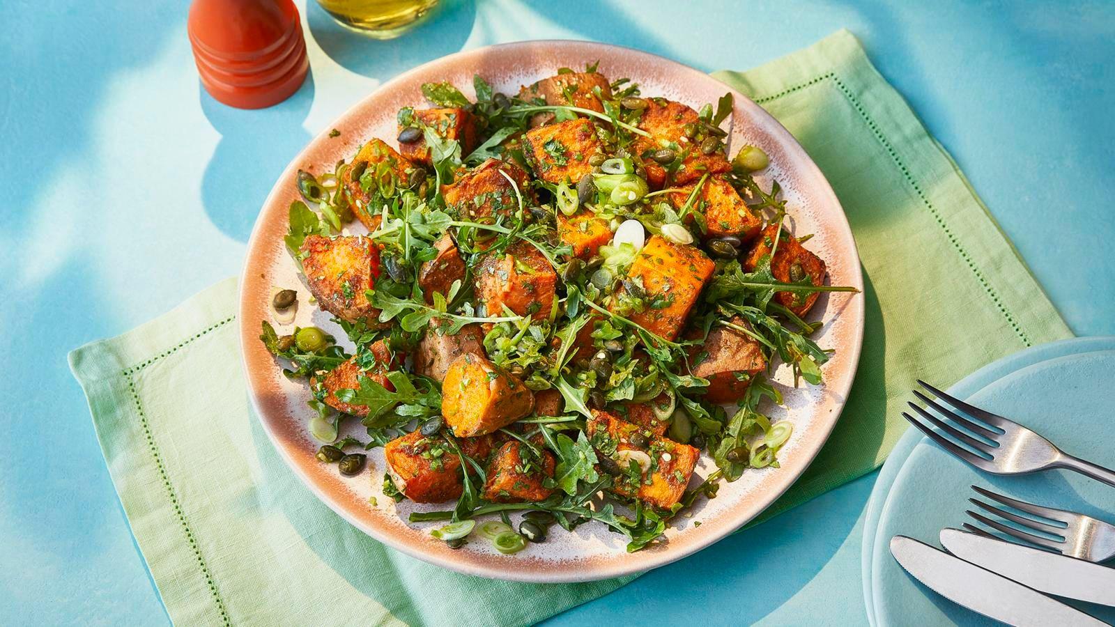 Sweet potato salad in a peach coloured bowl on a pale green linen napkin on a blue background