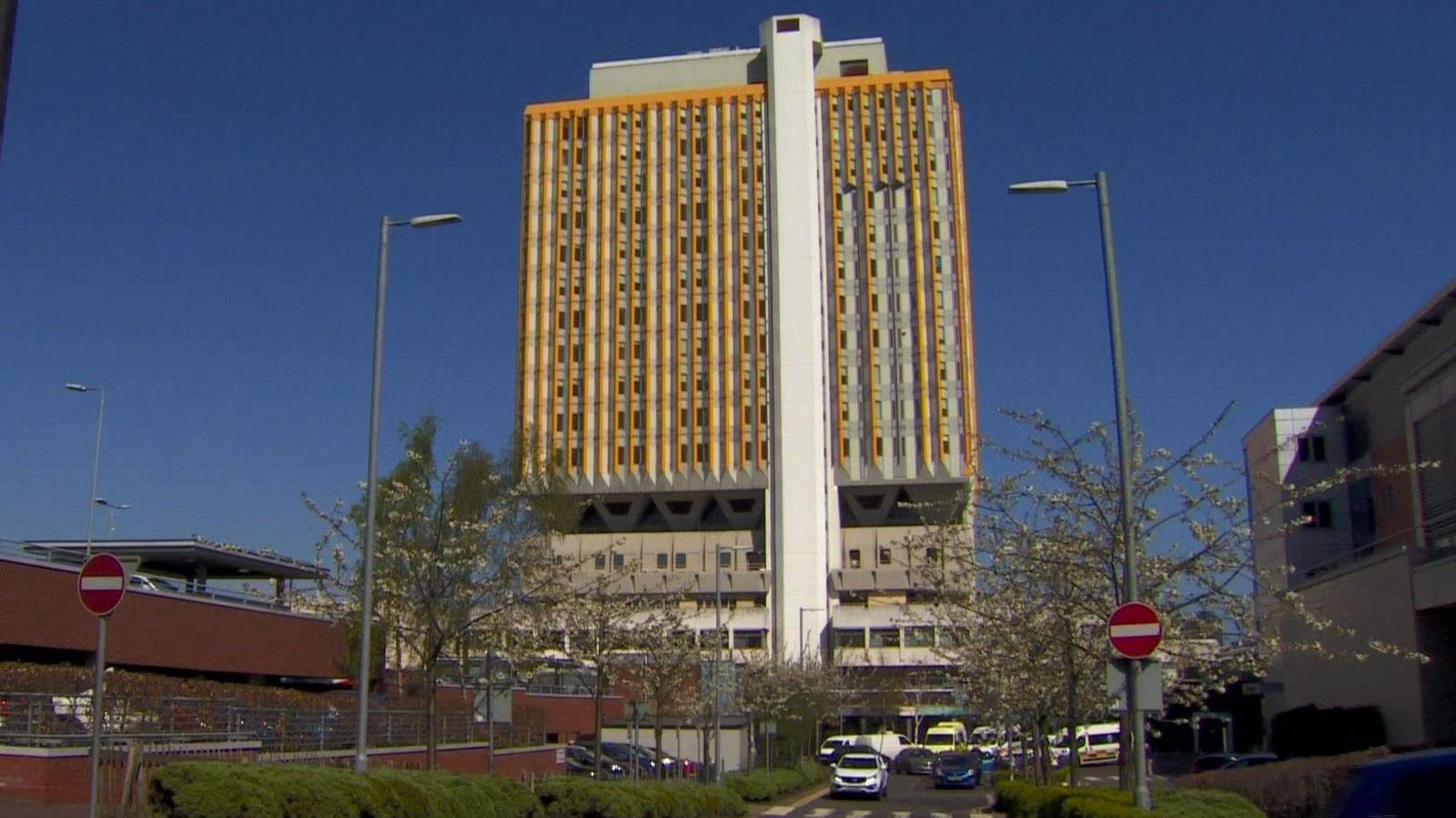 A yellow and grey tower block stand with lower red brick buildings in the foreground. 