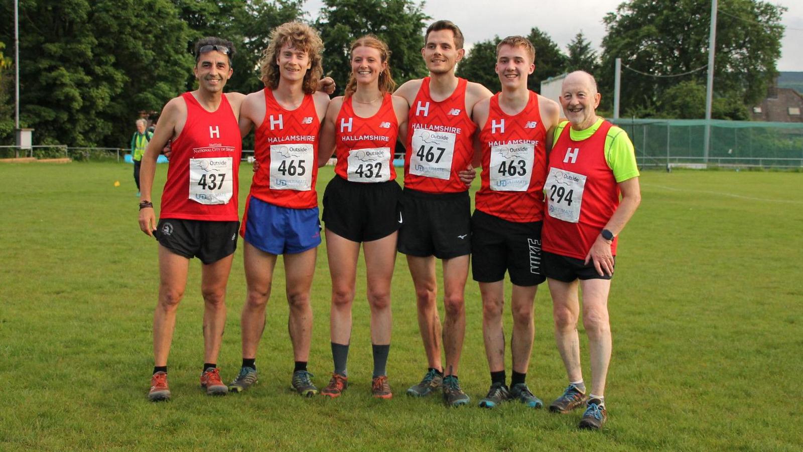 Six people wearing red vests standing with their arms over each other