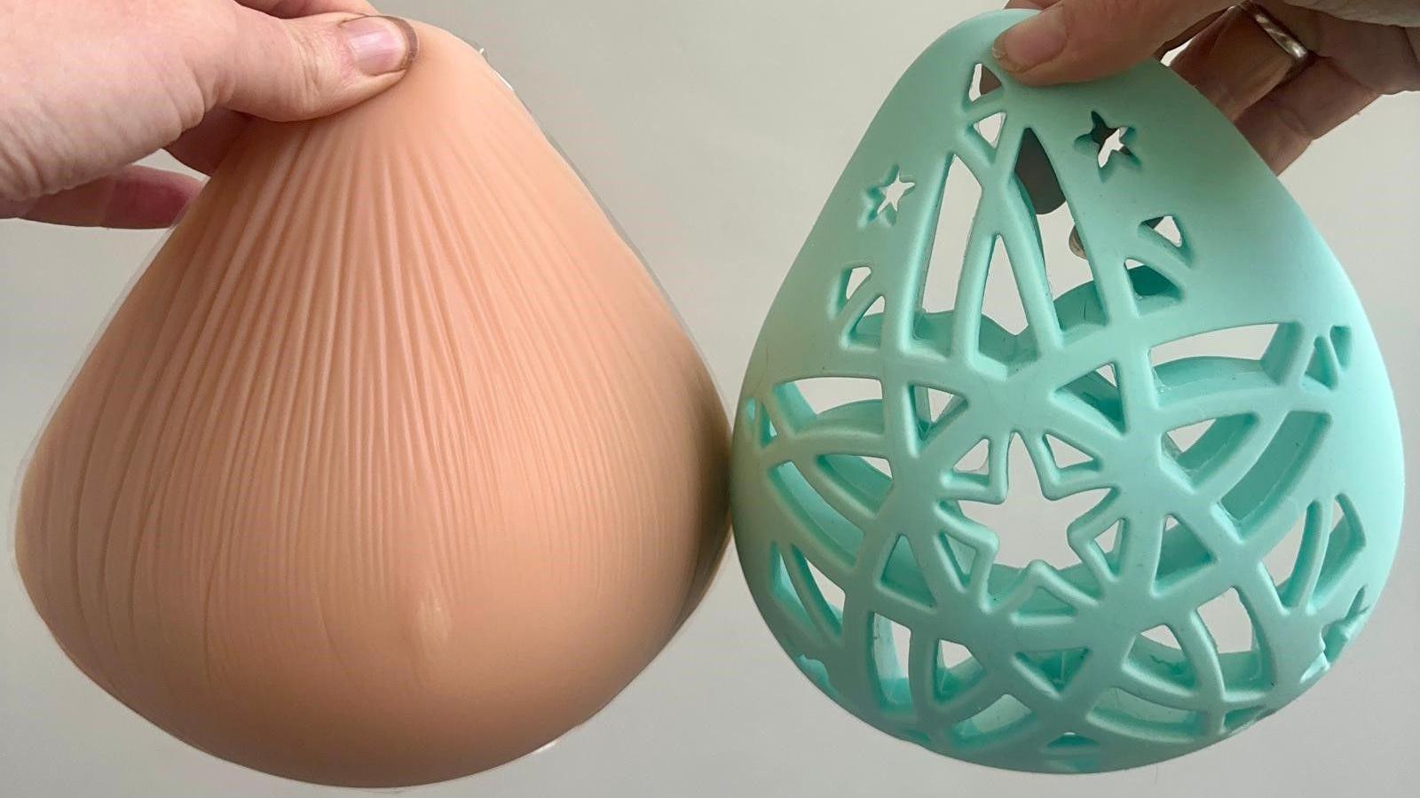 Hands are holding a breast prothesis that is heavier than the blue breast form that is made of silicone and designed with stars, it also is not padded, it keeps its shape. 