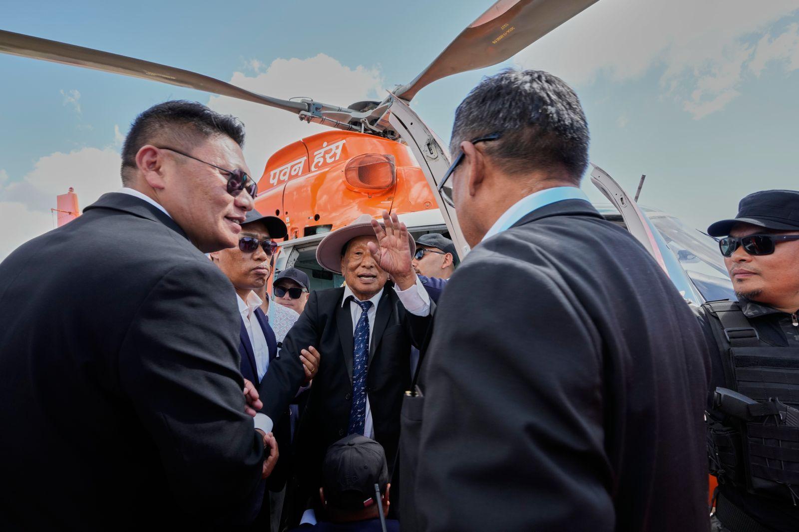 Dressed in a black coat, white short and blue tie, Thuingaleng Muivah waves at his supporters after getting out of the helicopter that brought him back home