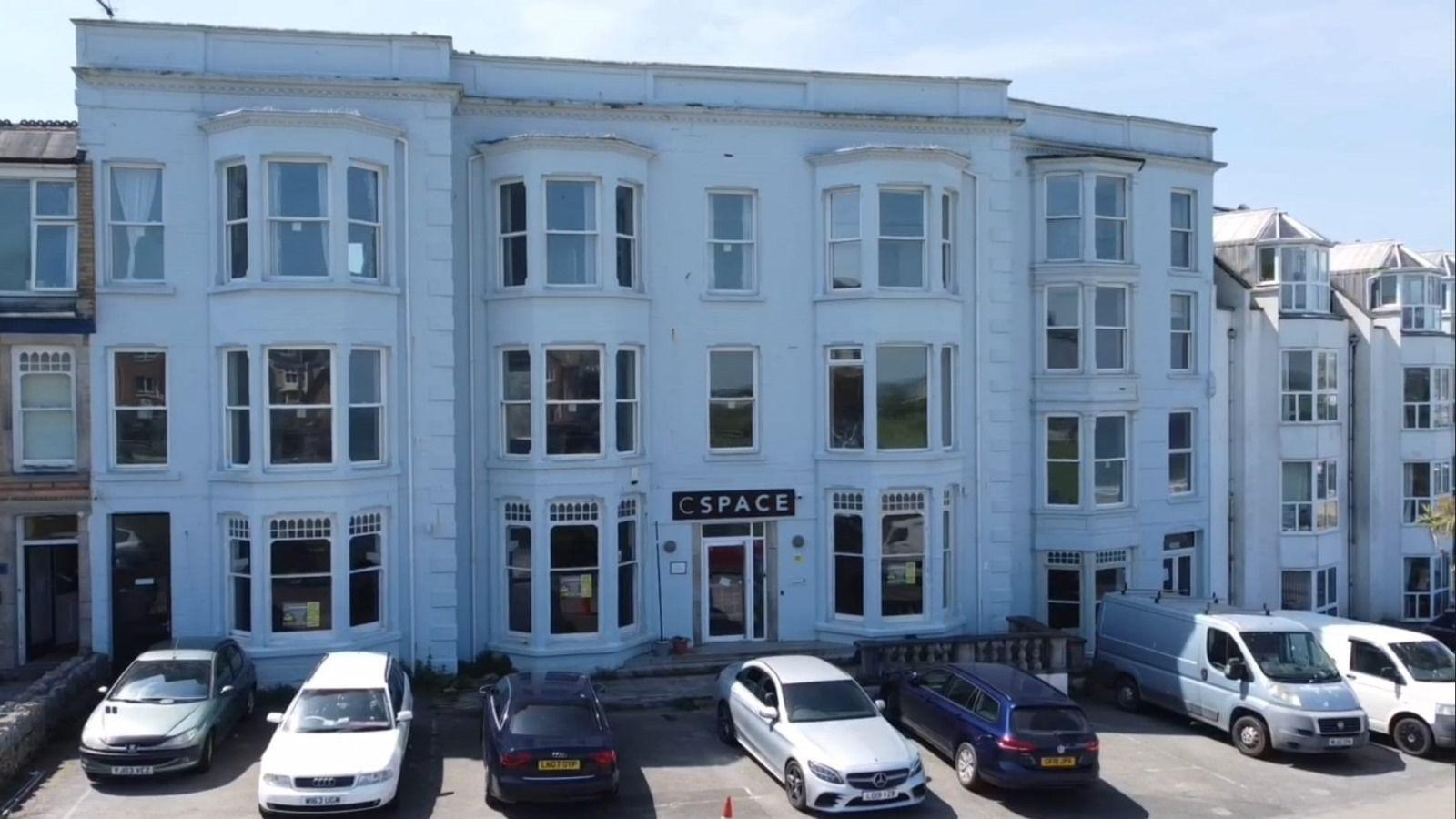 CSpace pictured. The property is a large white building, appearing to be Georgian in style. It has three storeys with six large bay windows and two smaller windows in the centre. There is a glass front door beneath a black rectangle sign reading "CSpace". 