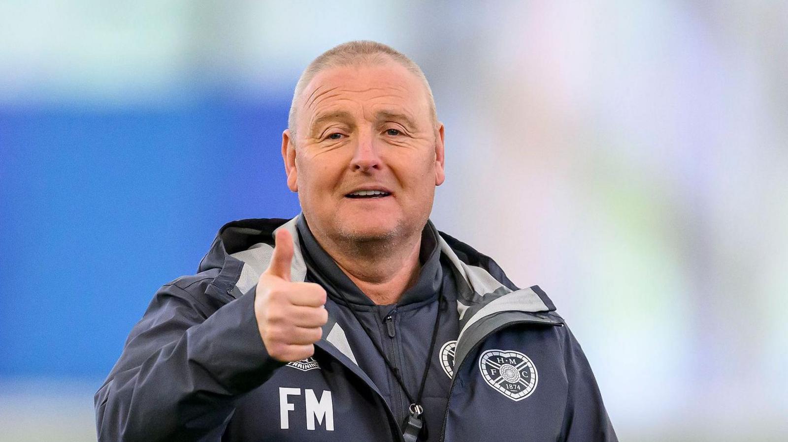 Frankie McAvoy, wearing a Hearts tracksuit with his initials on, gives a thumbs up to the camera