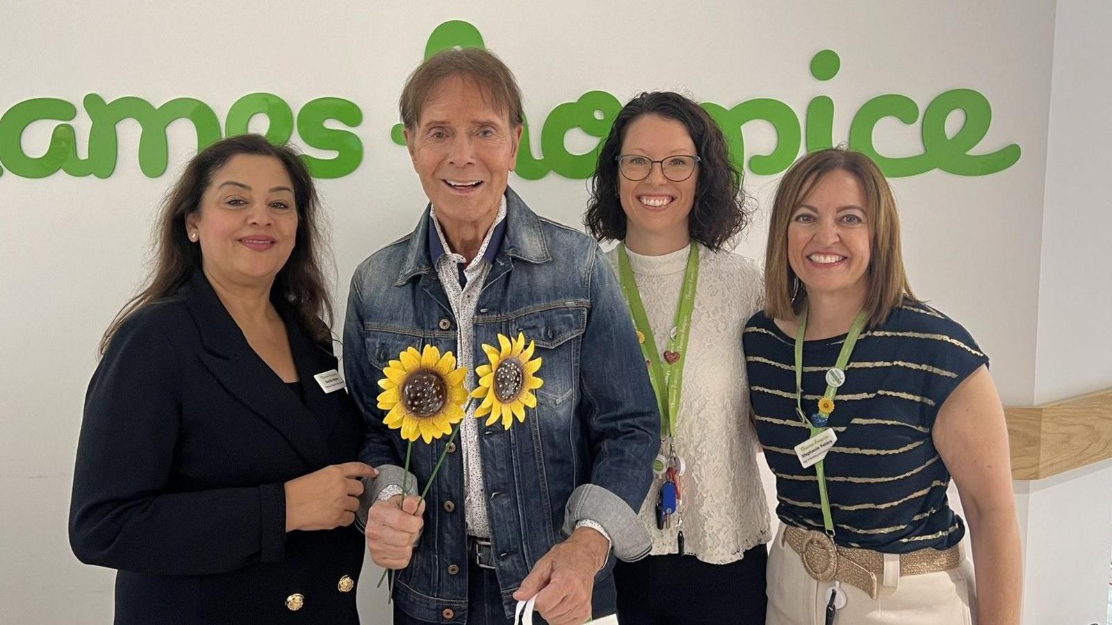 Sir Cliff (holding two sunflowers and wearing a denim jacket) poses with Sunita Arora, Jane Symmons, and head of marketing Stephanie Peters)