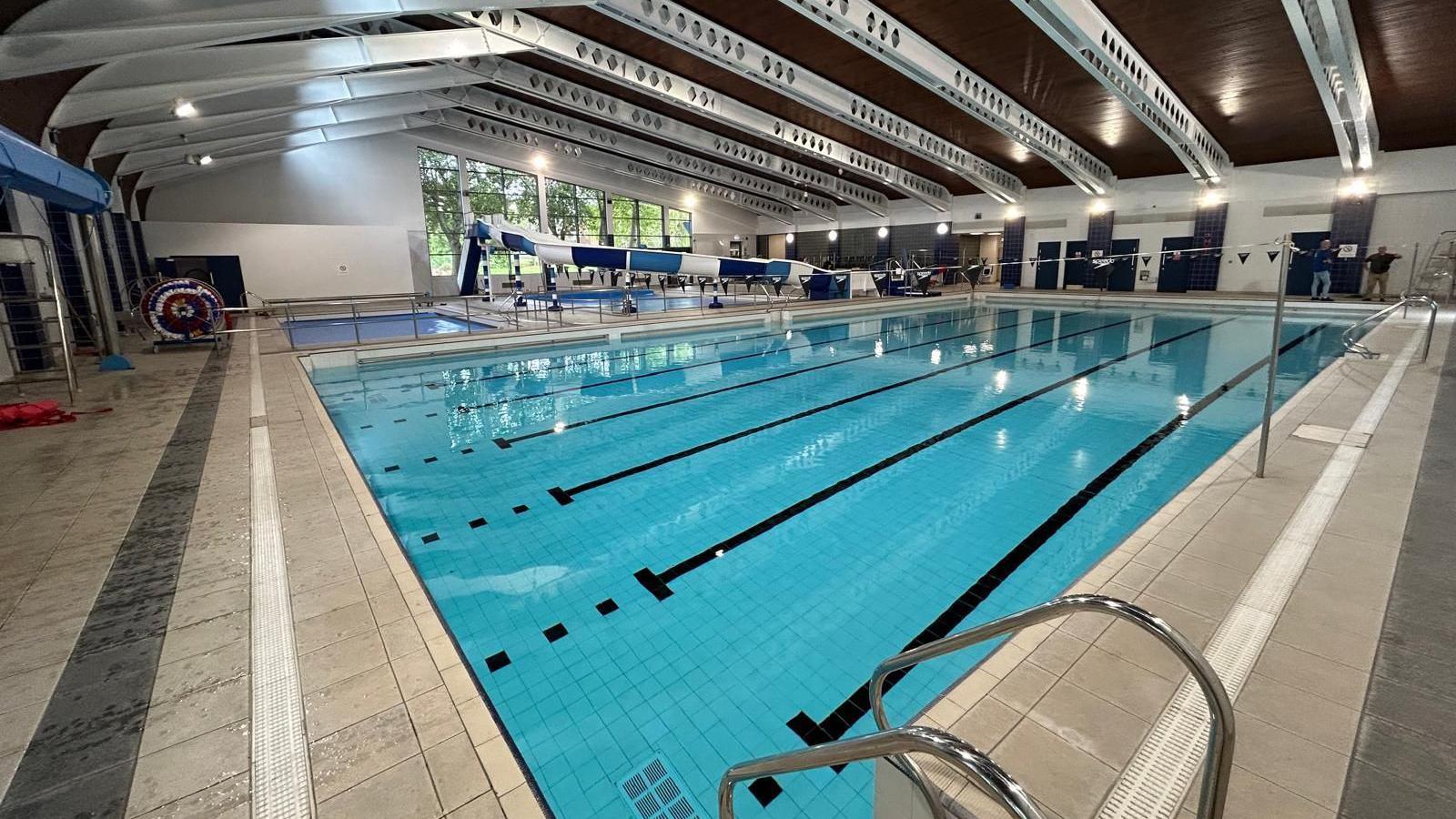 A wide shot of the swimming pool. The blue and white waterslide can be seen in the background as well as a smaller children's pool.