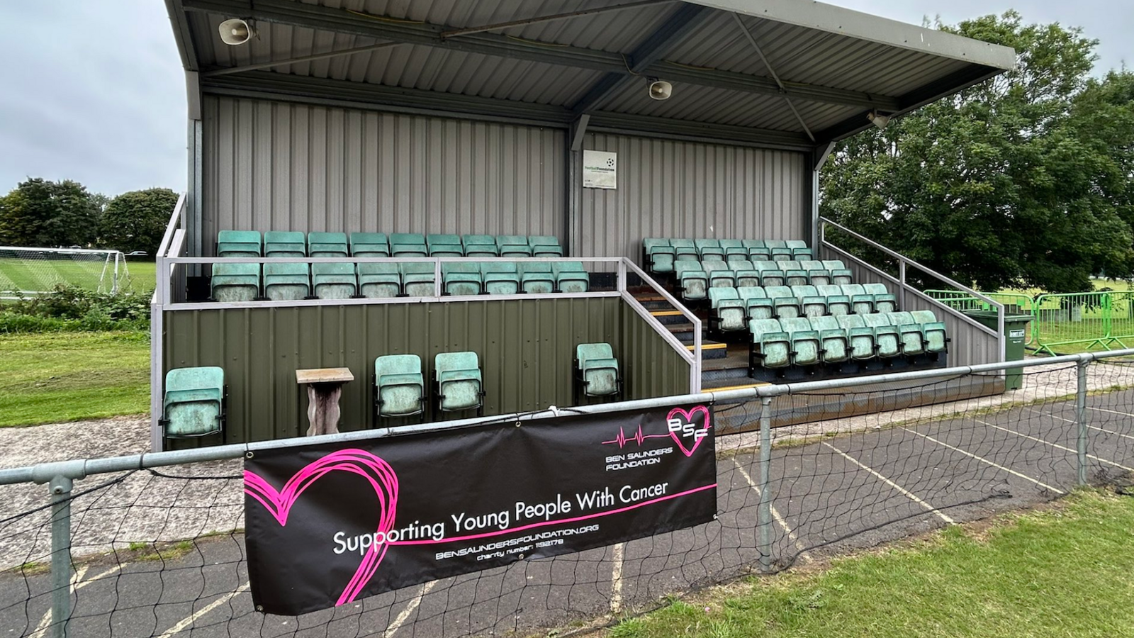 One of the boards at a football ground. The board is black with 'supporting young people with cancer' on it