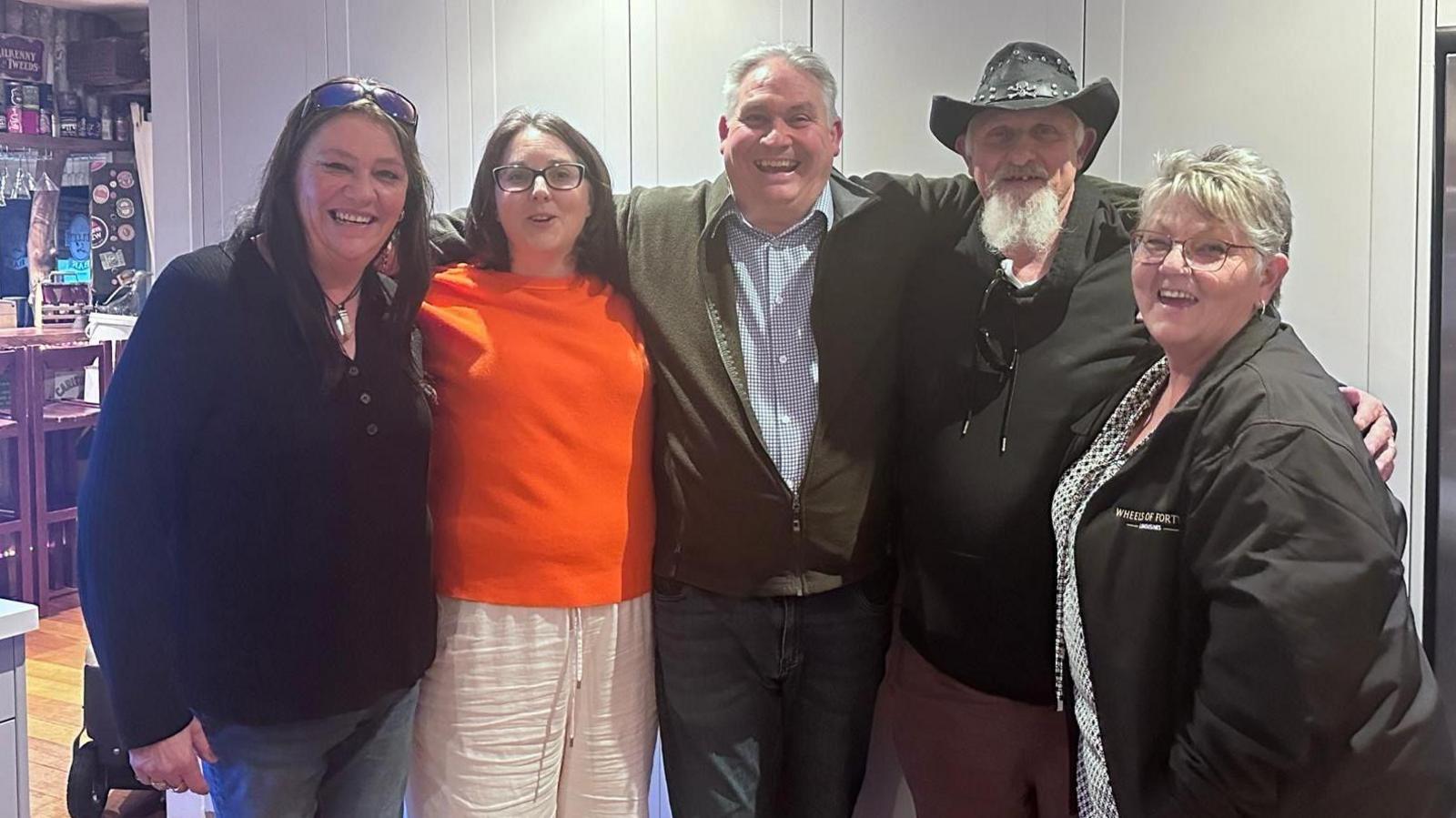 Five people lined up with their arms around each other's shoulders - Lateesha, Tina, Malcolm, Sean and Janette