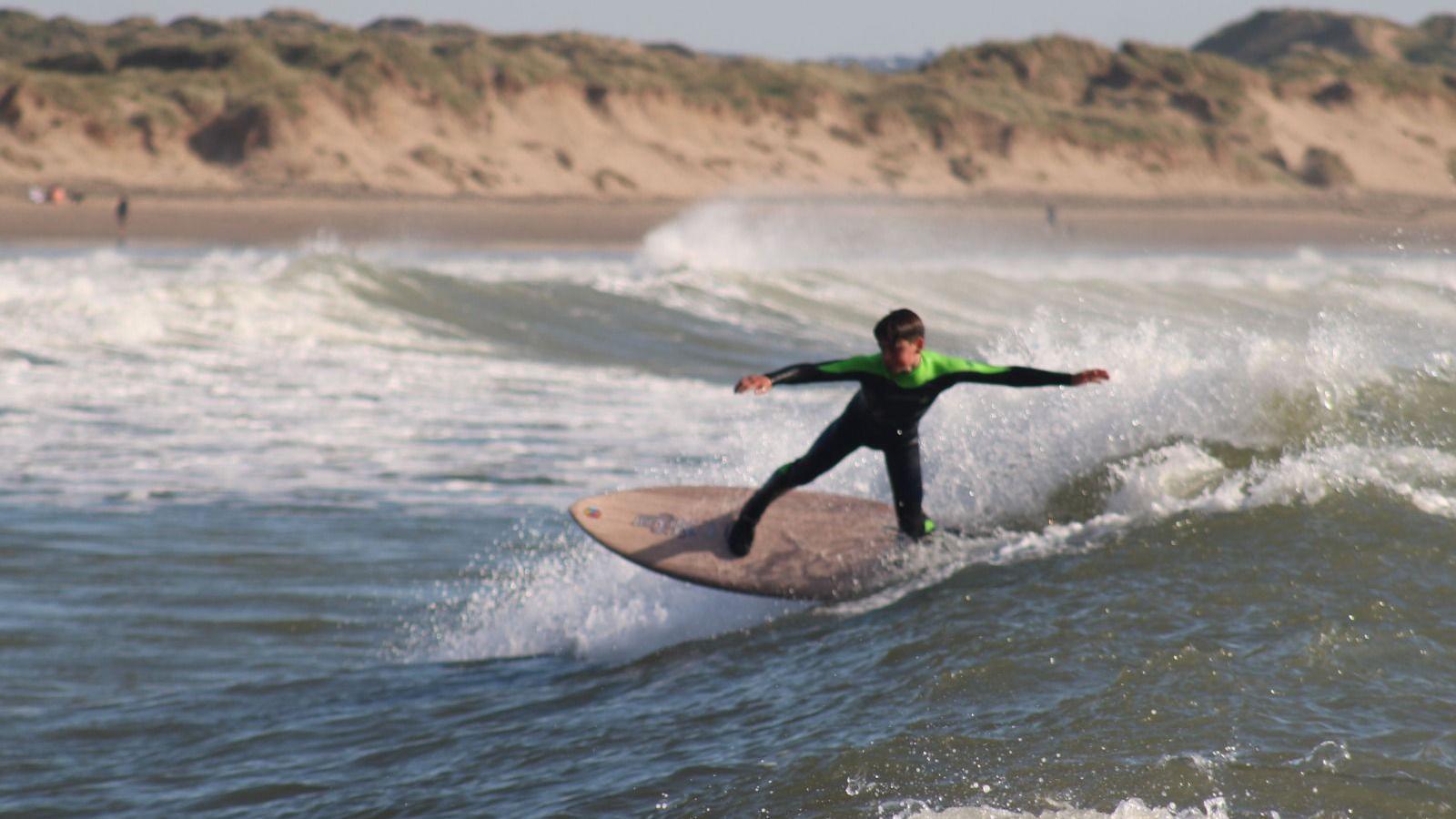 Oscar in a black and green wetsuit surfing