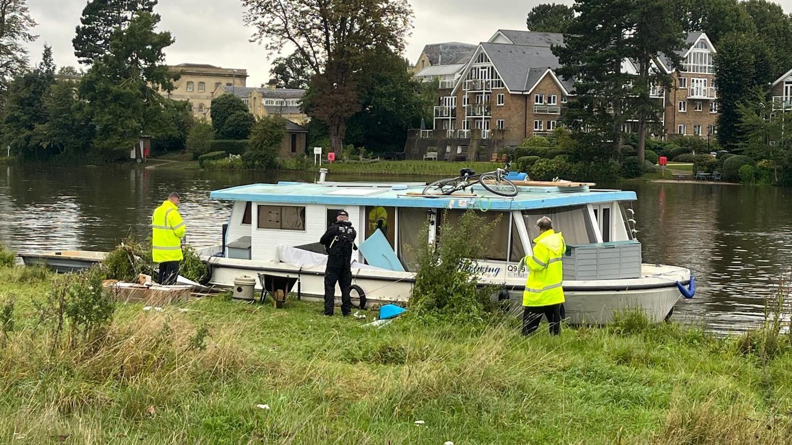 A blue and white boat is surrounded by police and other authorities in yellow high-visibility jackets 