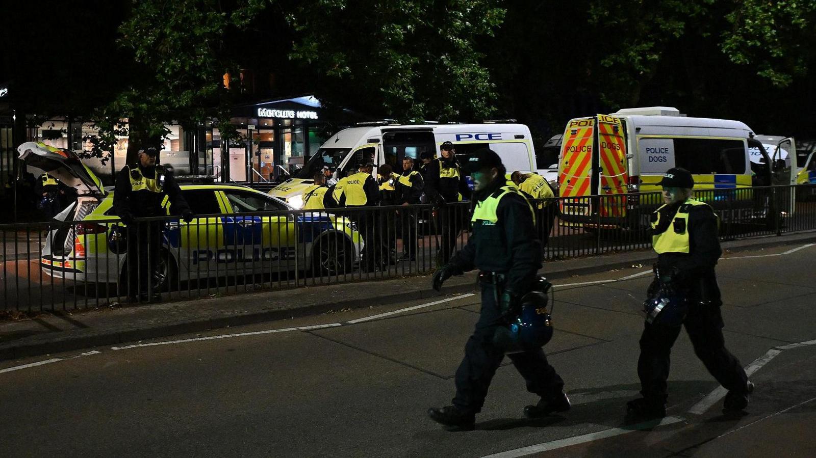 A line of police in riot gear stand by riot vans on Redcliffe Hill in Bristol outside the Mercure hotel, whose illuminated sign can be seen in the background