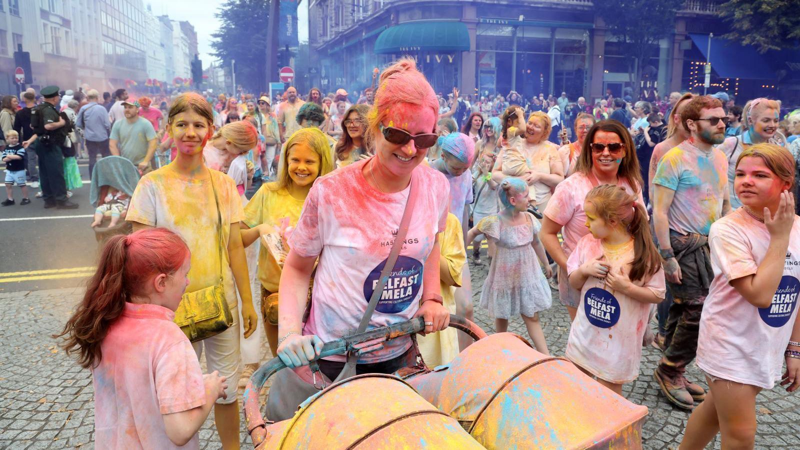 People walking in the parade covered in coloured paint powder.