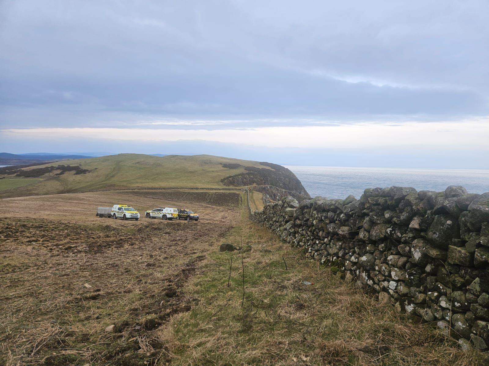 A number of rescue vehicles on grassland next to a dry stone wall on the Solway coast