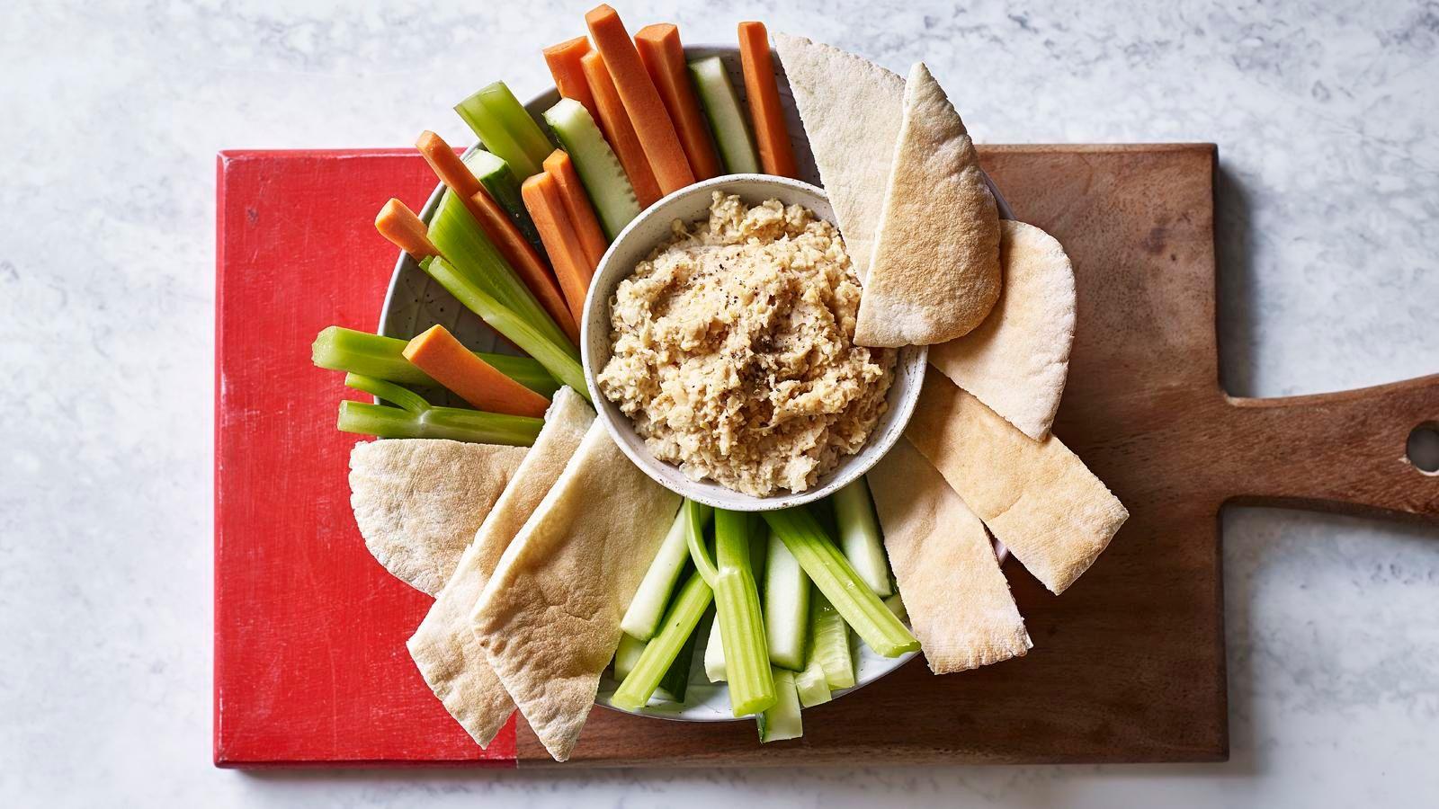 Hummus in a bowl surrounded by crudités and slices of pitta
