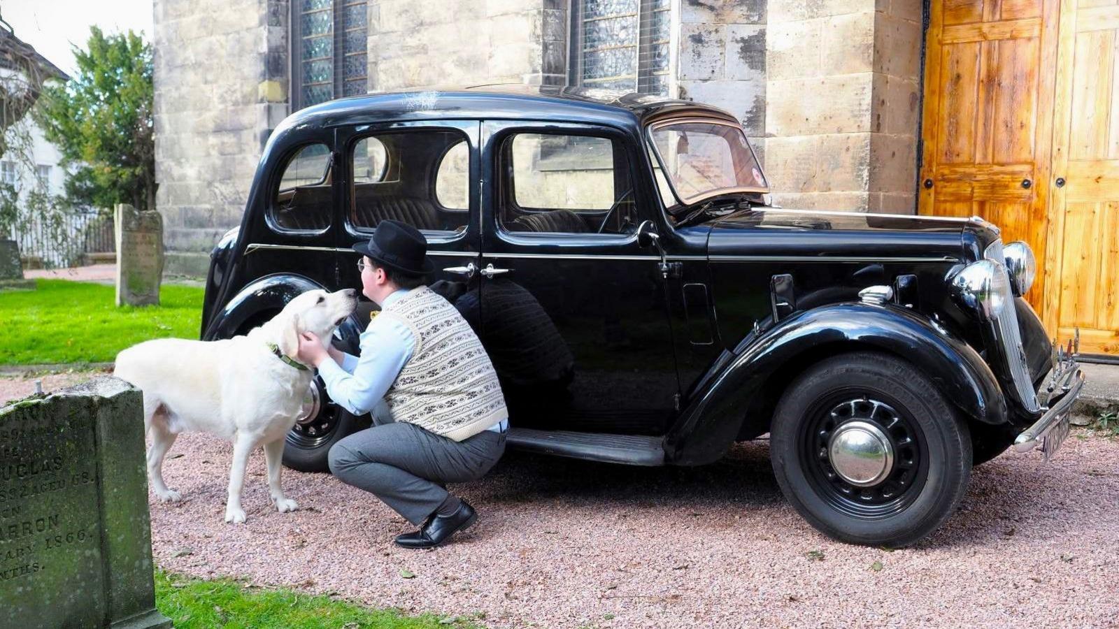 Callum petting his dog beside his car