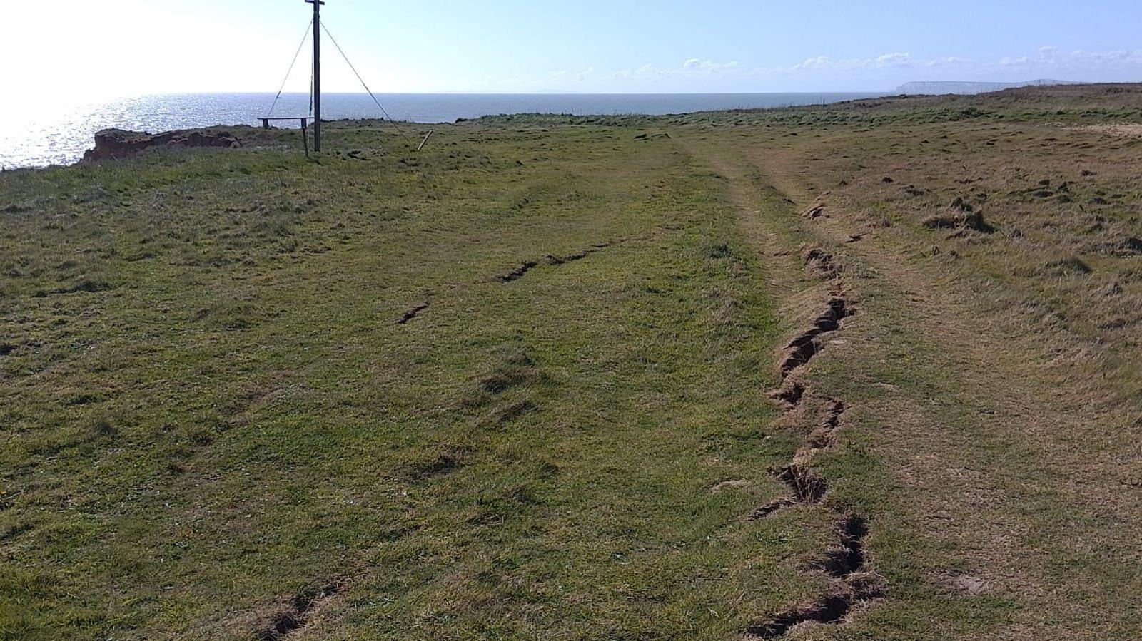 The same area, but it looks like a grassy area on the coast, with long cracks in the ground.
