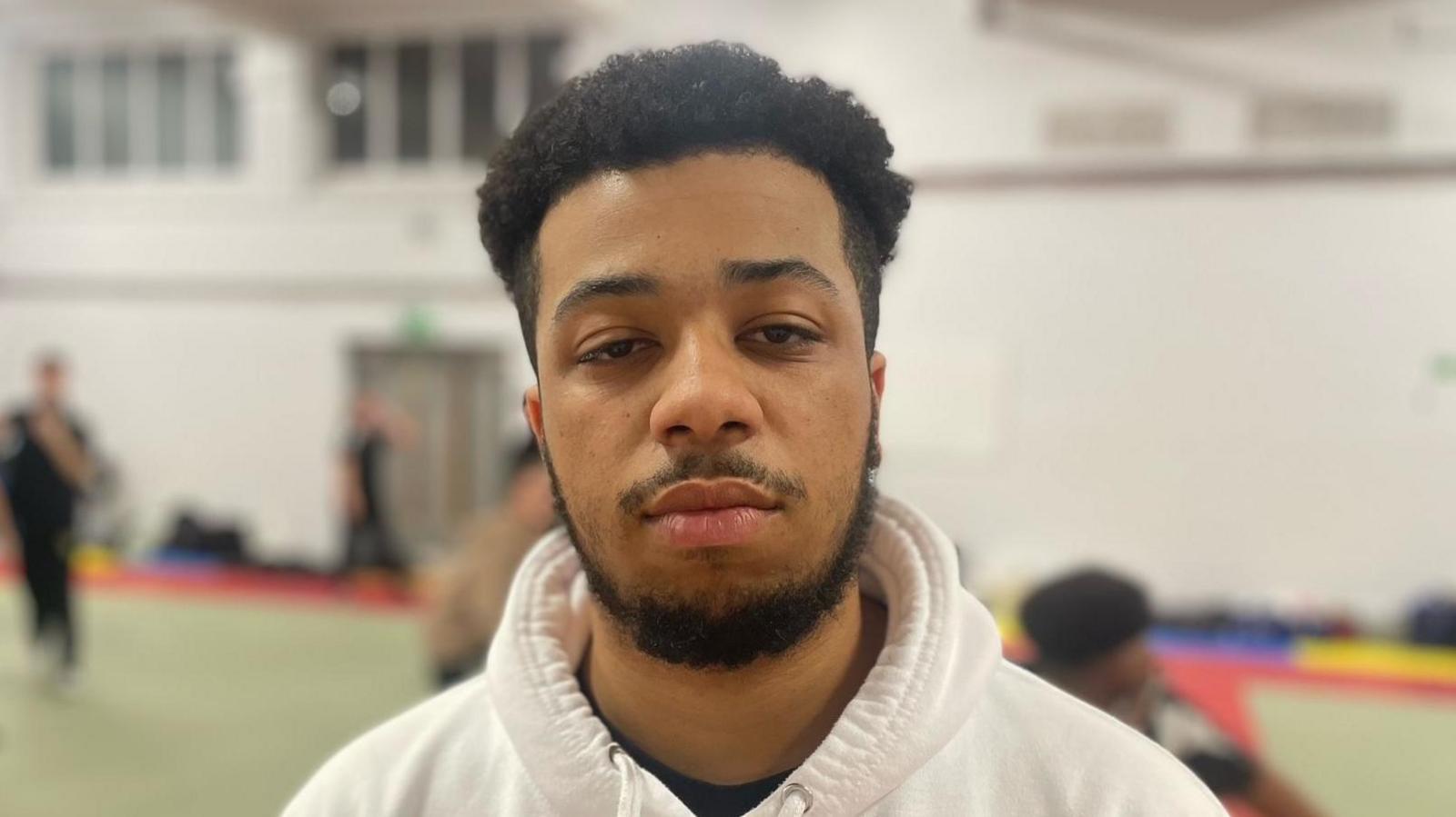 A young black man with a beard and white hoodie