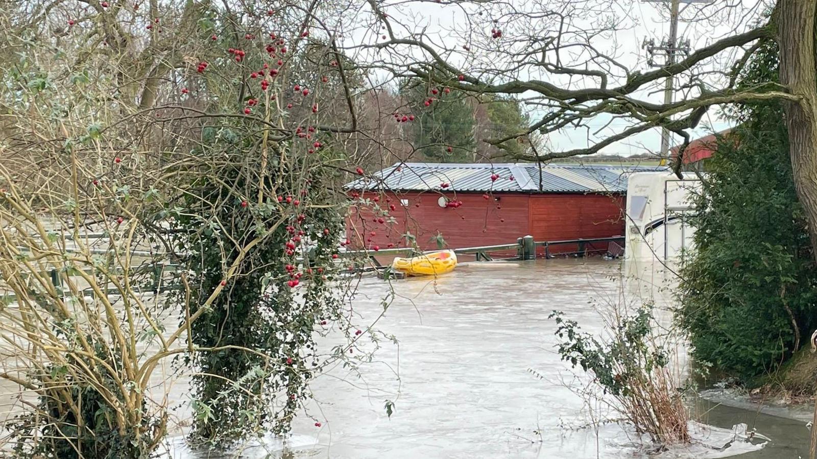 Icy flood water in a field. In the background a wooden stable block surrounded by flood water