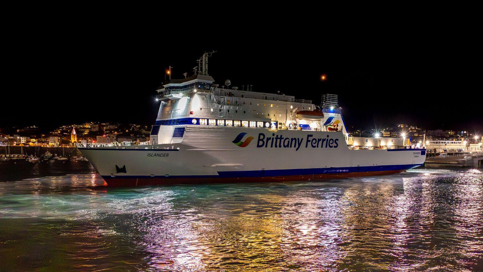 The Islander, a large white ferry in Guernsey's St Peter Port Harbour. It has a Brittany Ferries logo on the side and has lights on it.