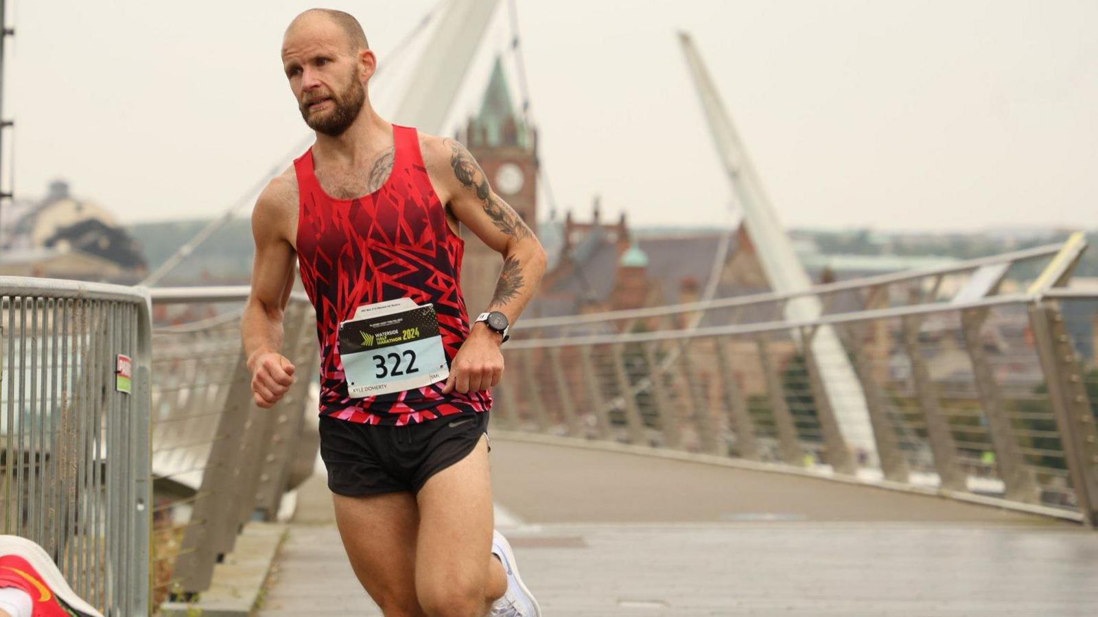 Kyle running over a bridge. He is wearing a red top and black shorts.